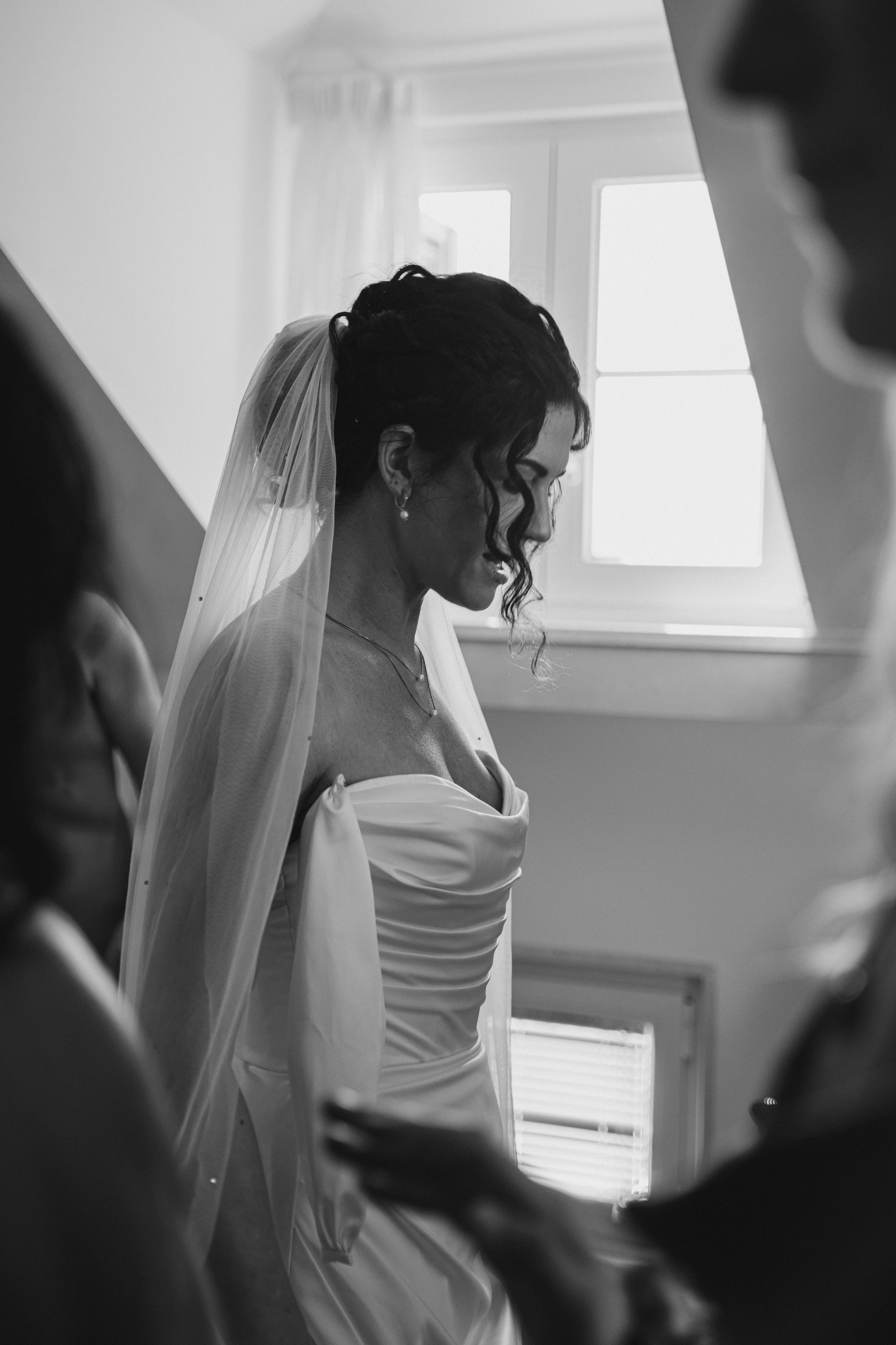 A bride in a wedding dress and veil smiling as she prepares for her wedding, surrounded by other women.