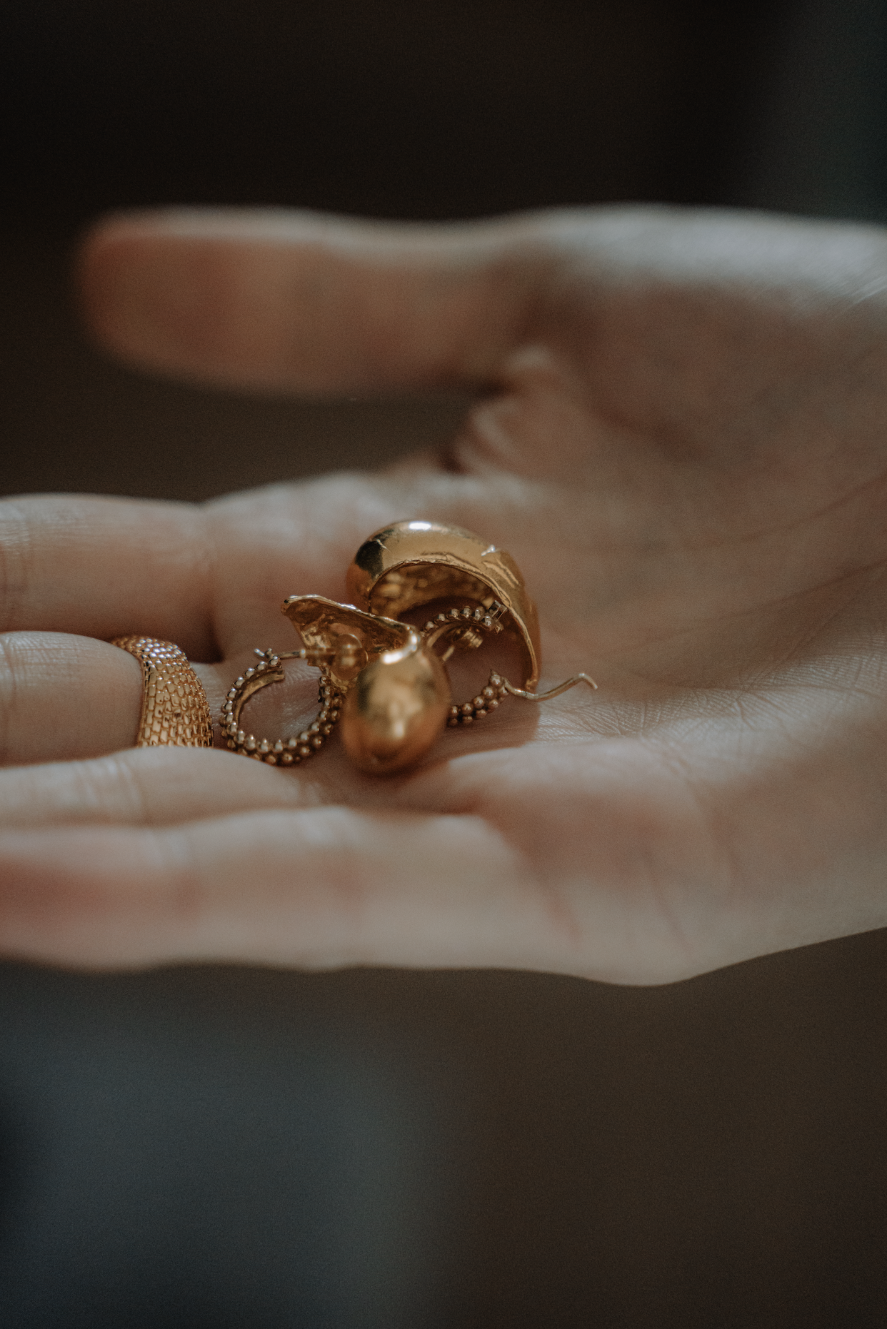 Close-up of a hand holding gold jewelry, including earrings and a ring.