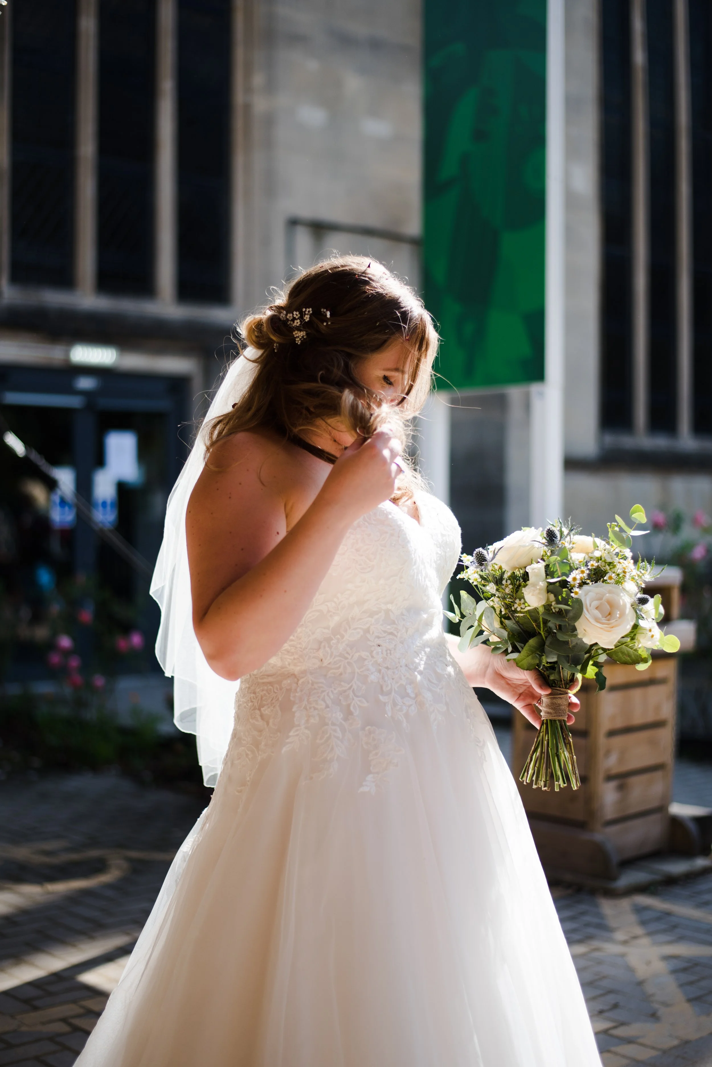 A bride in a white wedding dress holding a bouquet of white and green flowers, standing outdoors.