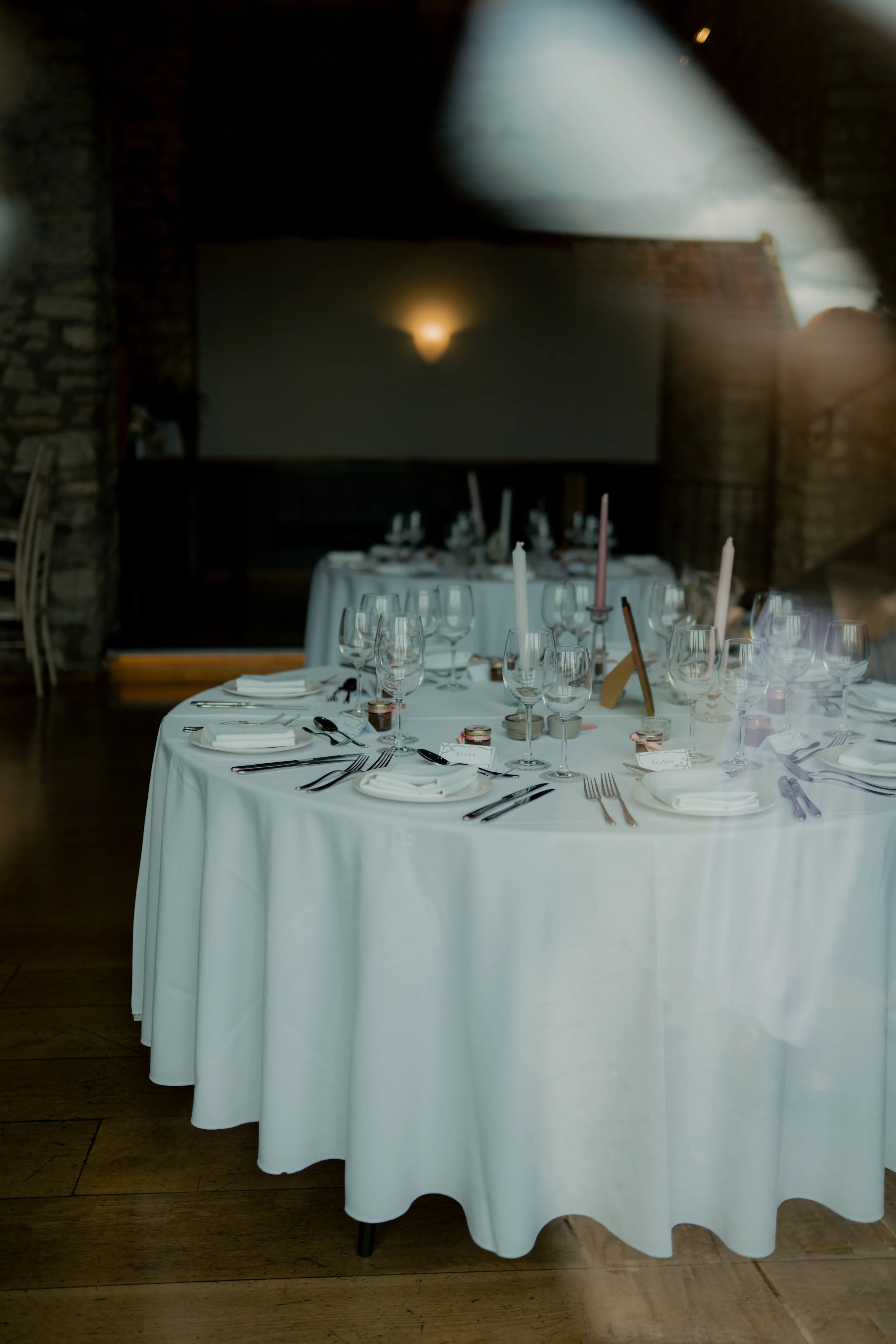 Elegant banquet table set with white tablecloth, multiple wine glasses, cutlery, plates, and candles in a dimly lit room.