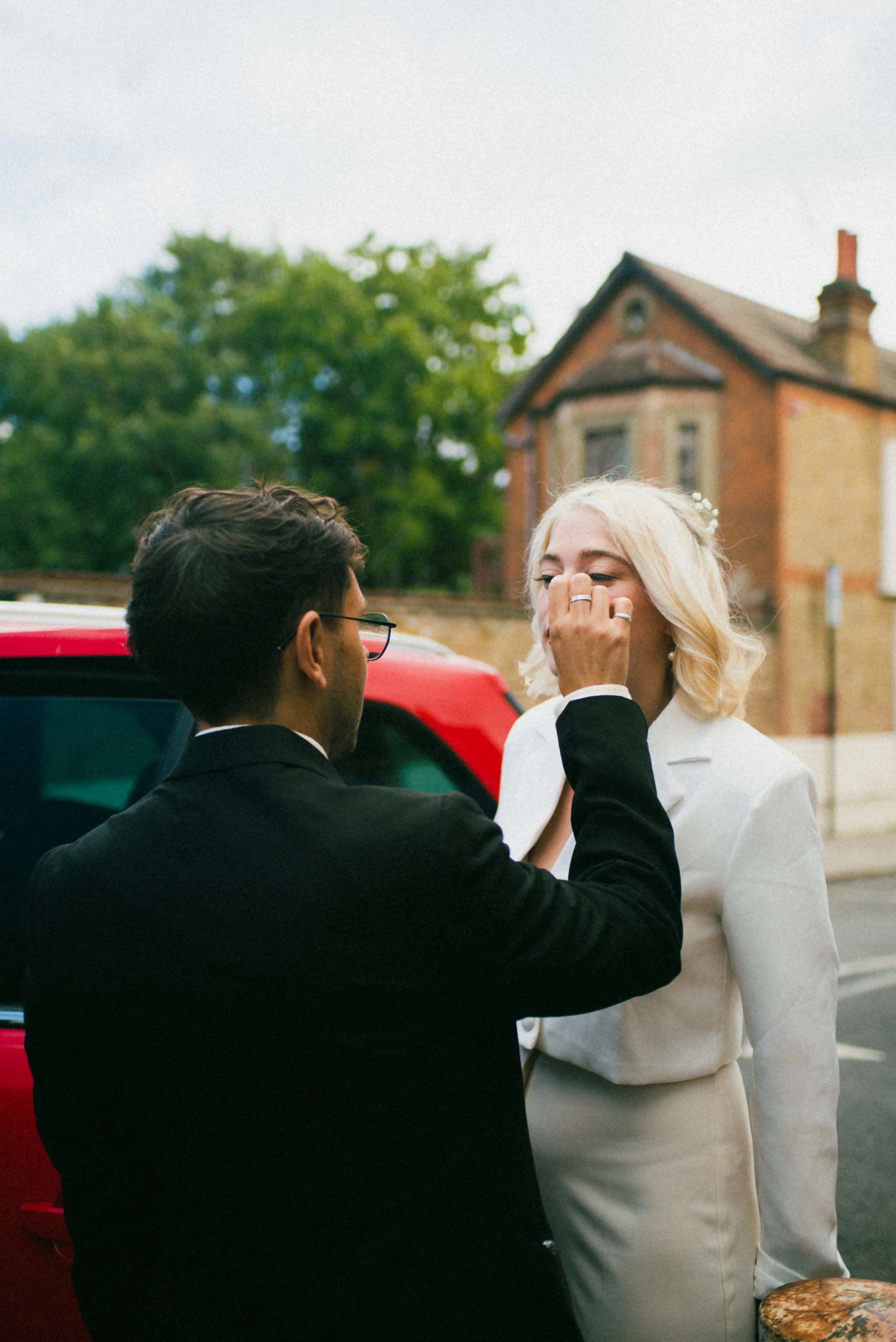 A man in a black suit is putting a ring on a woman's finger during a wedding or engagement celebration outdoors.