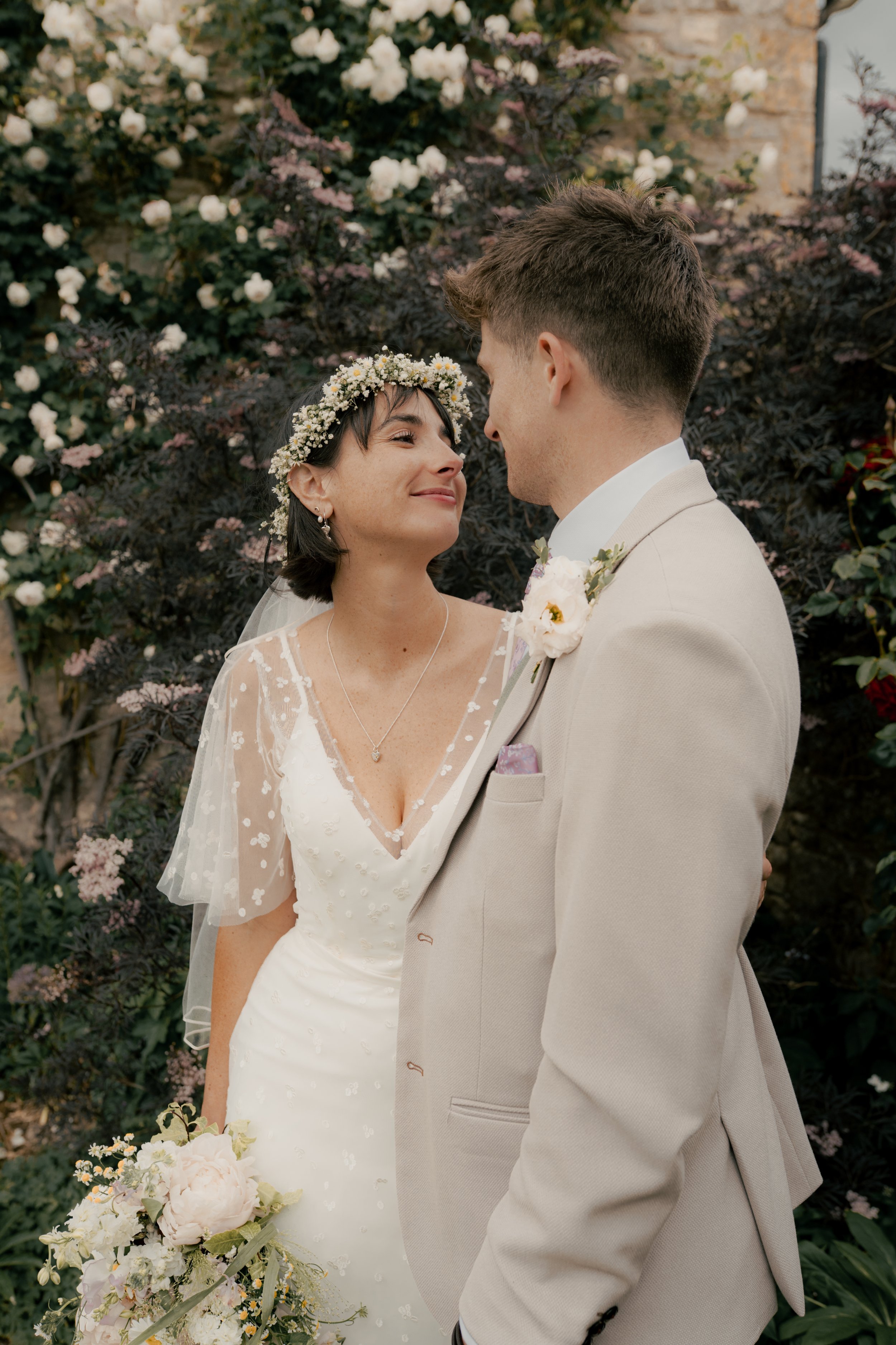 A bride and groom looking at each other in a garden setting, surrounded by flowers and greenery.
