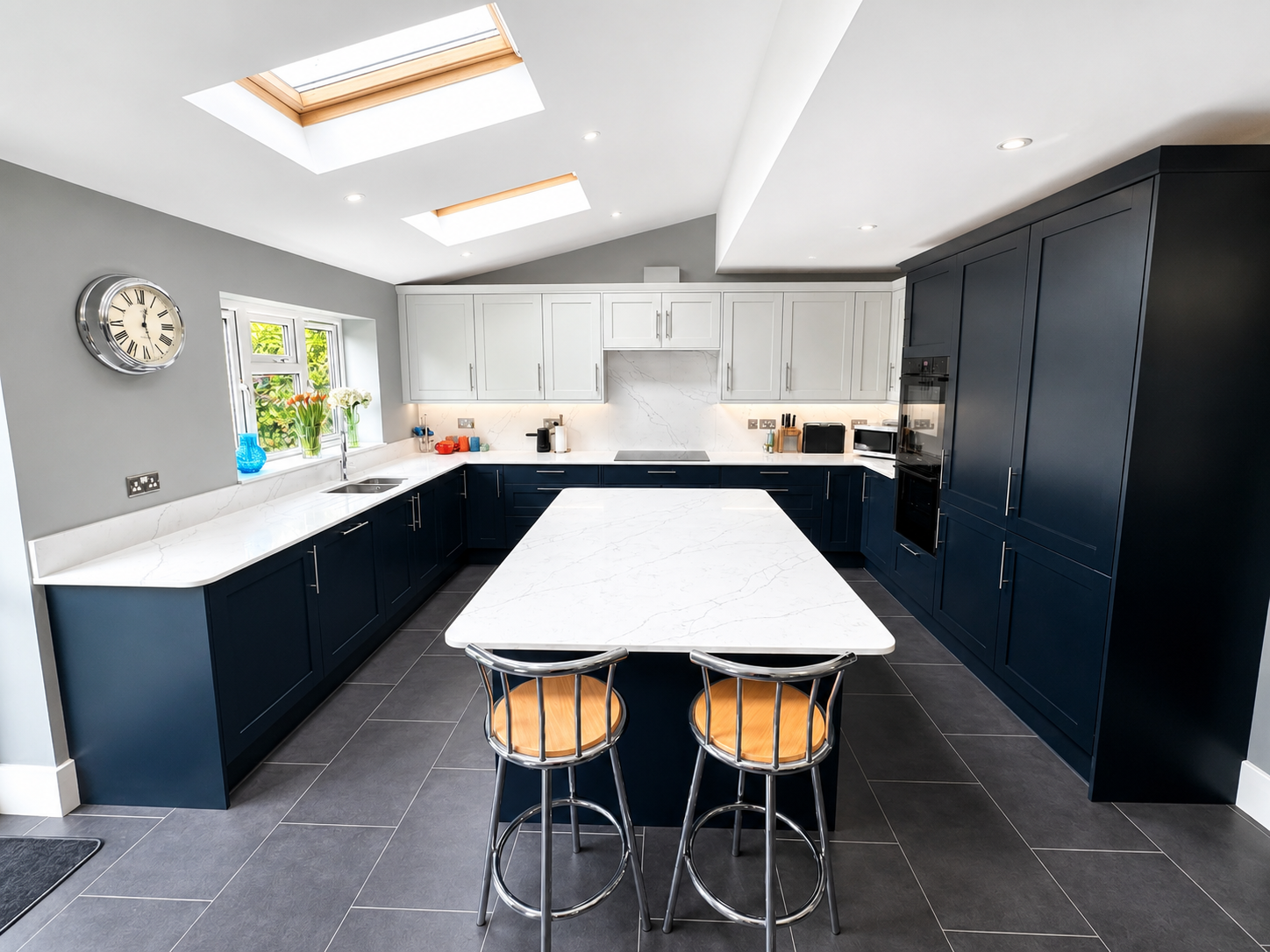 Two-tone navy and white kitchen gin bar in Wokingham with illuminated glazed wall units, wine cooler, white quartz worktop and grey tiled flooring by Blacktail Kitchens.