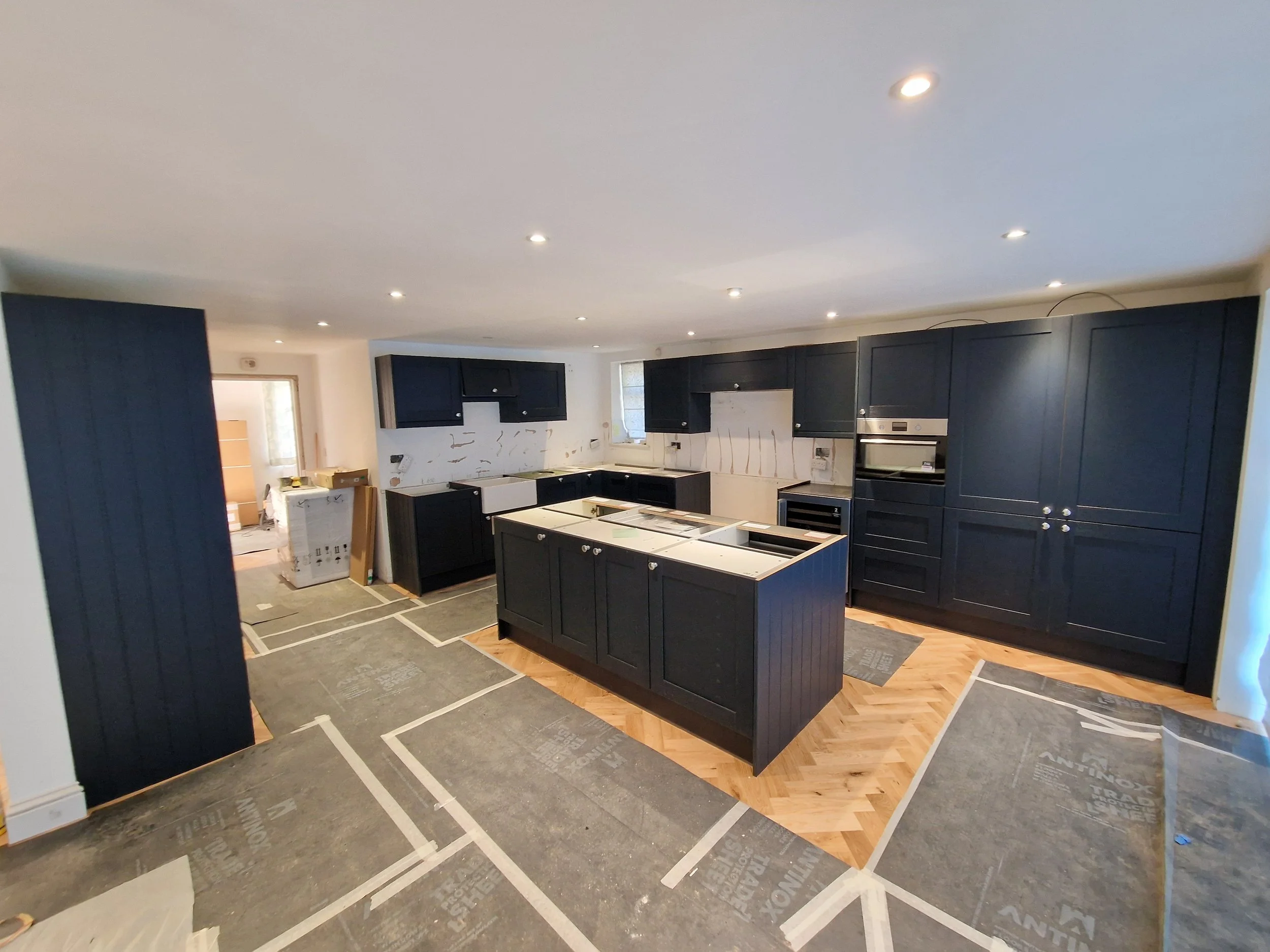 Kitchen with dark blue cabinets, an island, appliances, and under-construction elements with protective floor covering.