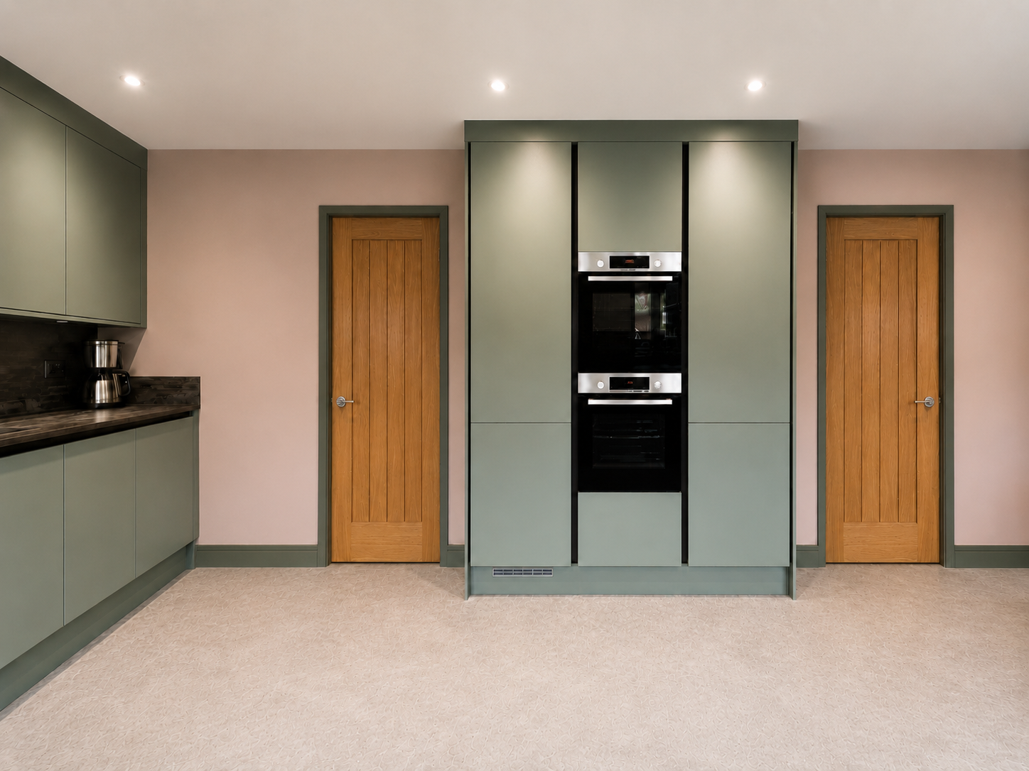 Central tower units in Warfield kitchen with integrated double oven, true handleless green cabinetry, warm pink walls and stone-effect LVT flooring.