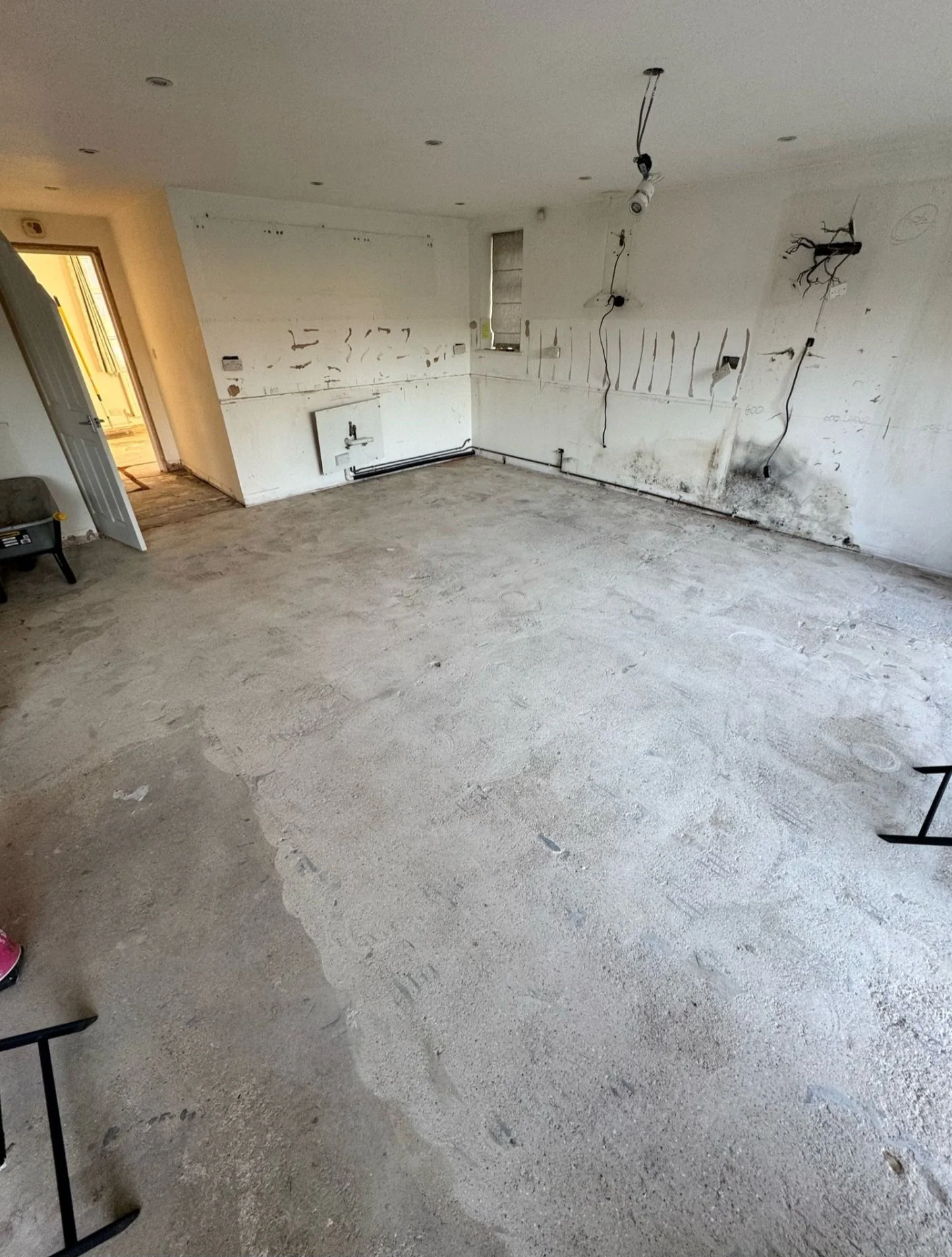 Kitchen renovation before installation with unfinished walls, exposed wiring, and a dirty concrete floor.