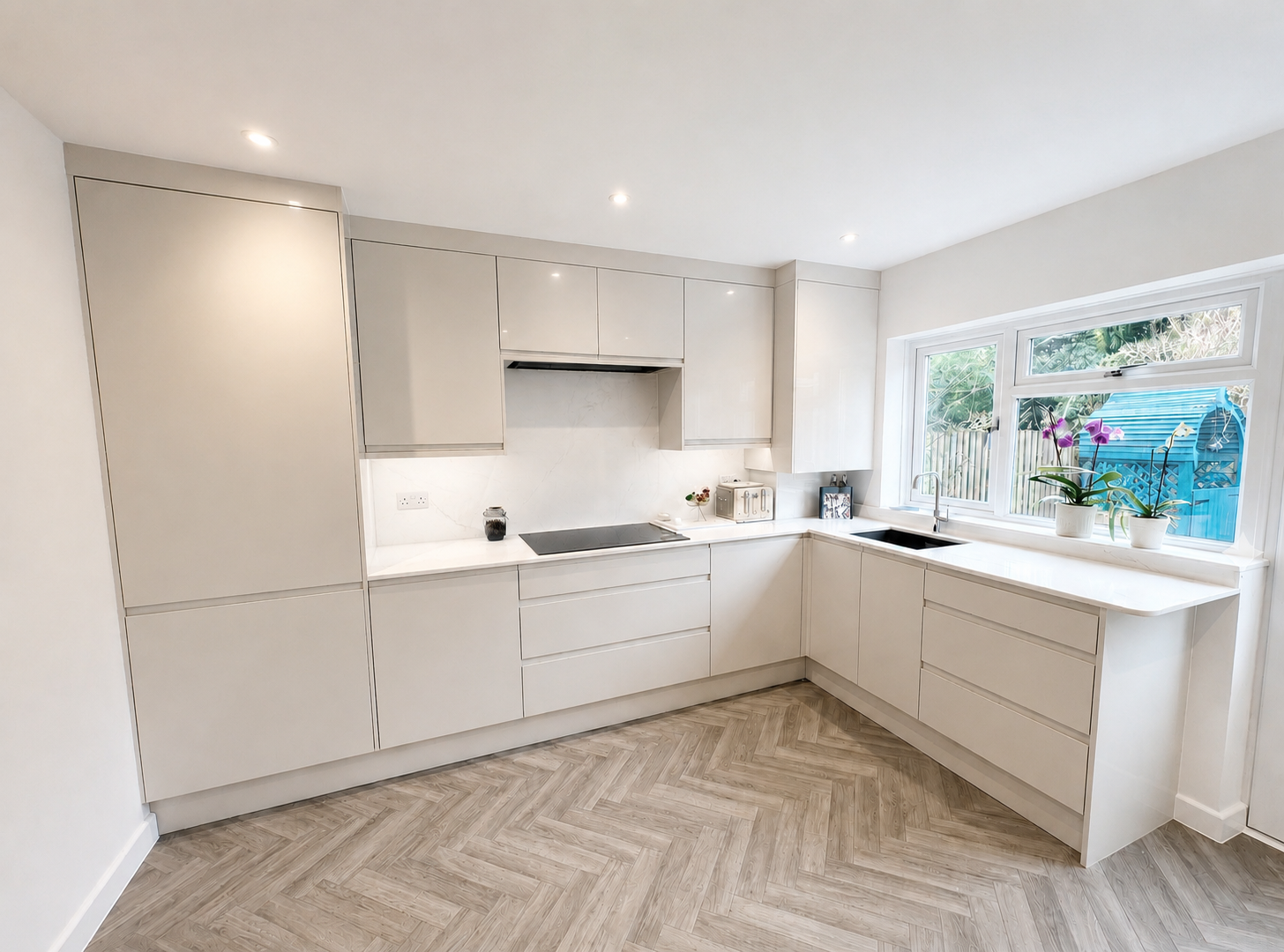 Light cream inset handle kitchen in Sunningdale with white quartz worktops, full-height matching splashback, undermount sink and herringbone LVT flooring by Blacktail Kitchens.