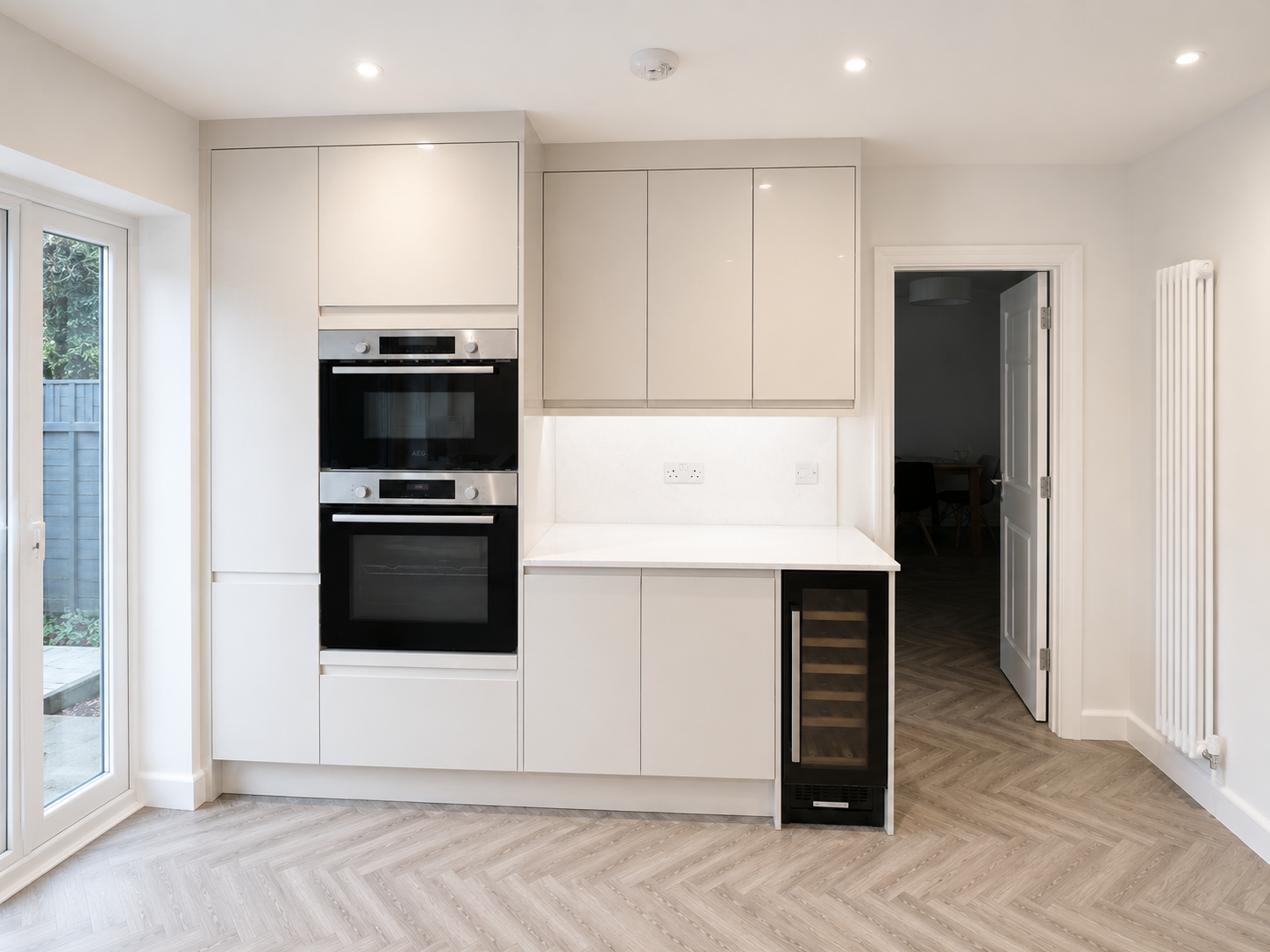 Handleless kitchen installation in Sunningdale with integrated double ovens, wine cooler, marble-effect worktop, tall storage units and herringbone LVT flooring by Blacktail Kitchens.