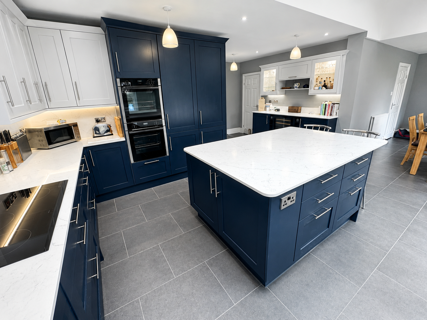Two-tone navy and white kitchen in Wokingham with a central island, white quartz worktops, integrated appliances, skylights and grey LVT flooring by Blacktail Kitchens.