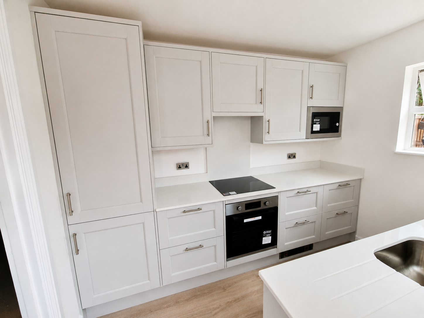 Porcelain white shaker kitchen installation in Bracknell with tall storage units, built-in oven, hob, compact microwave housing and white quartz worktops.