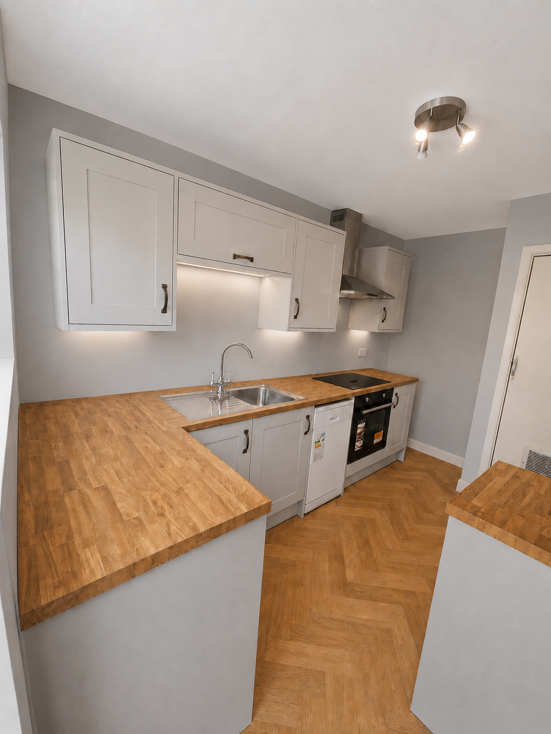 Shaker kitchen installation in Camberley with wood-effect worktops, LVT herringbone flooring, built-in oven, hob, extractor, sink and under-cabinet lighting.