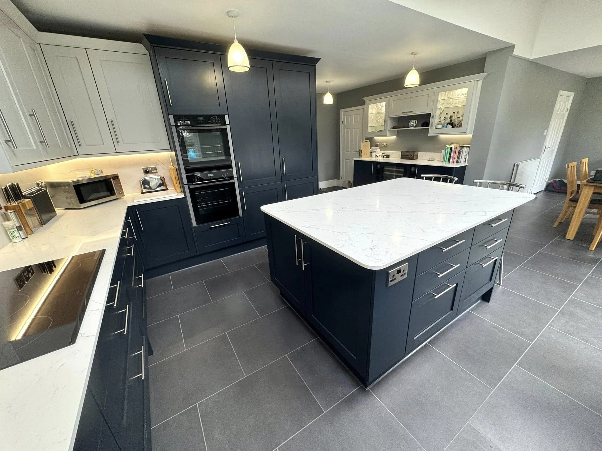 Modern kitchen with navy blue cabinets, a white marble island, gray tiled flooring, and pendant lighting.