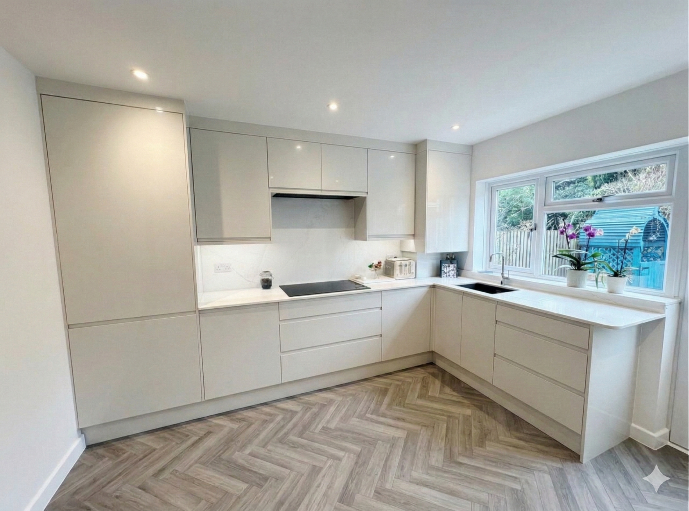 Modern, minimalist kitchen with white cabinetry, marble countertops, window with a view of outdoors, potted orchid plant on the window sill, and wooden flooring with herringbone pattern.