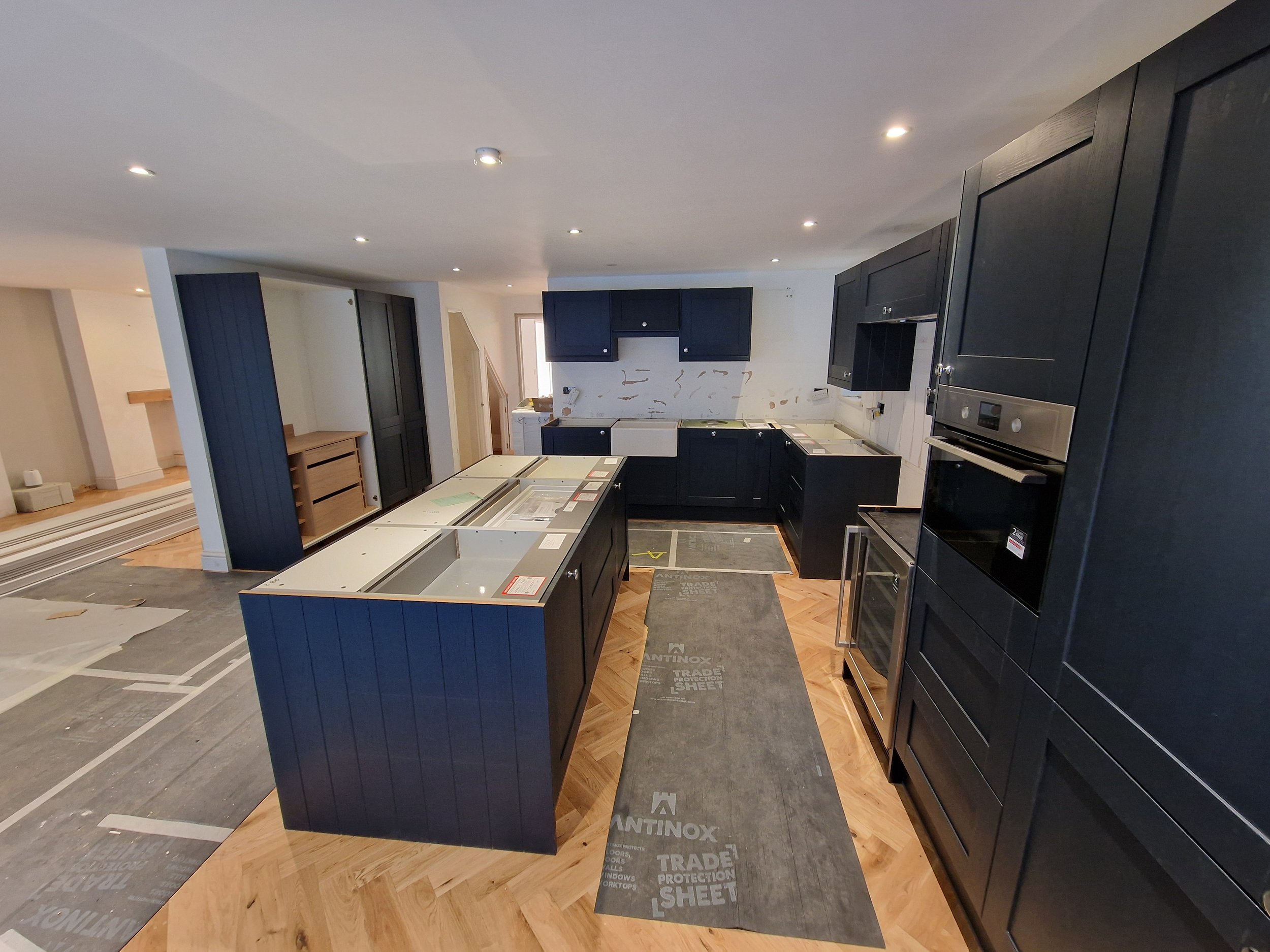 Kitchen renovation progress with black cabinetry, a kitchen island, and protective coverings on the floor.