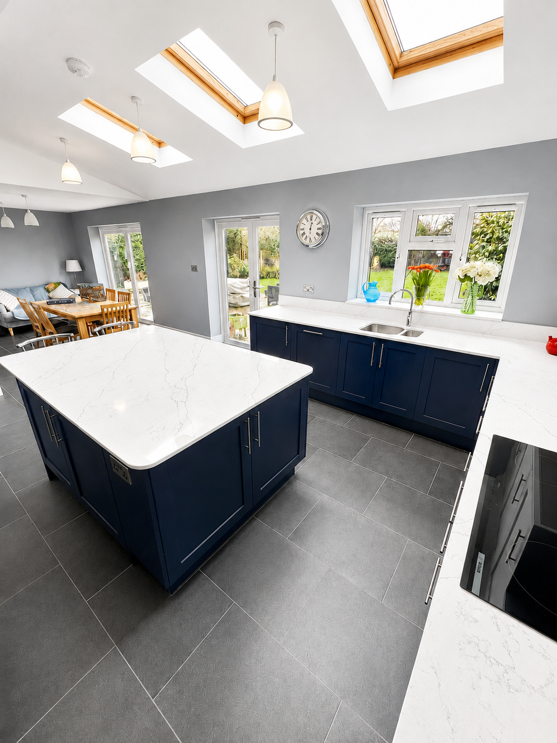 Wokingham kitchen installation with navy base units, white wall units, large quartz island, integrated appliances, gin bar area and grey LVT flooring by Blacktail Kitchens.