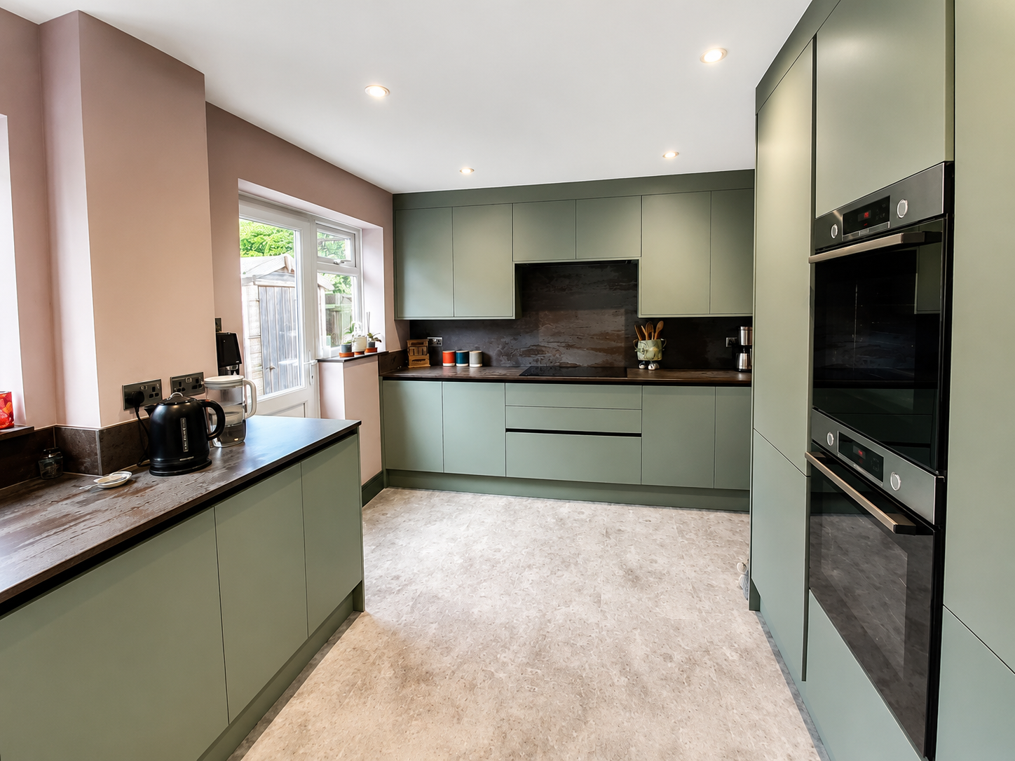 Modern kitchen with green cabinets, black countertops, a window, and built-in ovens.