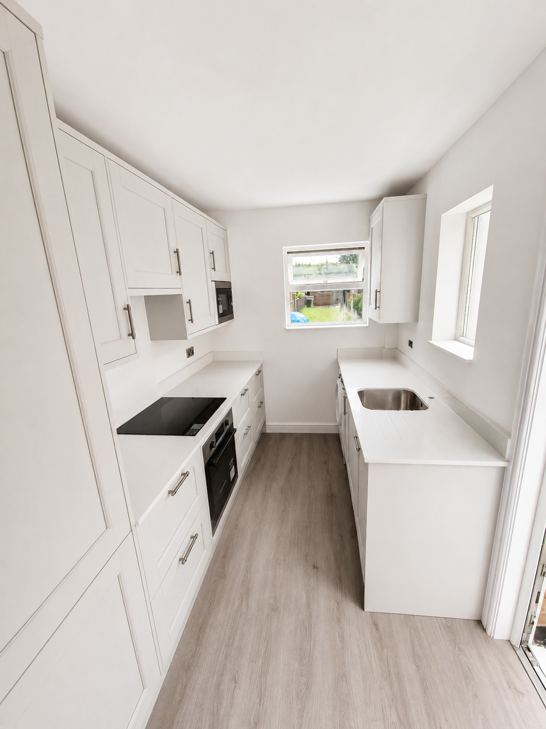 Porcelain white fitted kitchen in Bracknell with white quartz worktops, undermount sink, quartz drainer grooves, integrated appliances and wood-effect LVT flooring.