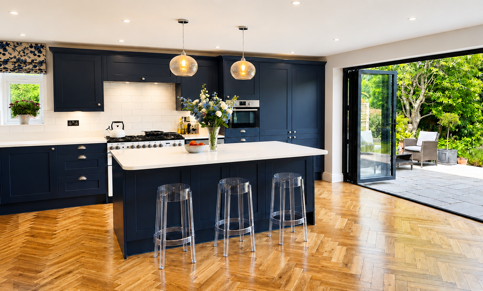 Navy shaker kitchen in Sonning with a large white worktop island, pendant lighting, clear bar stools, herringbone wood flooring and bi-fold doors to the garden by Blacktail Kitchens.