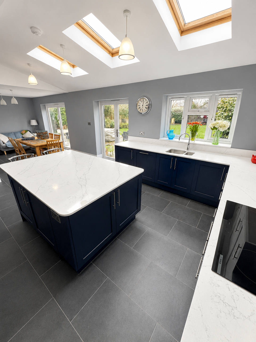 Navy kitchen in Wokingham with a large quartz island, skylights, sink run, grey tiled flooring and open-plan dining area by Blacktail Kitchens.