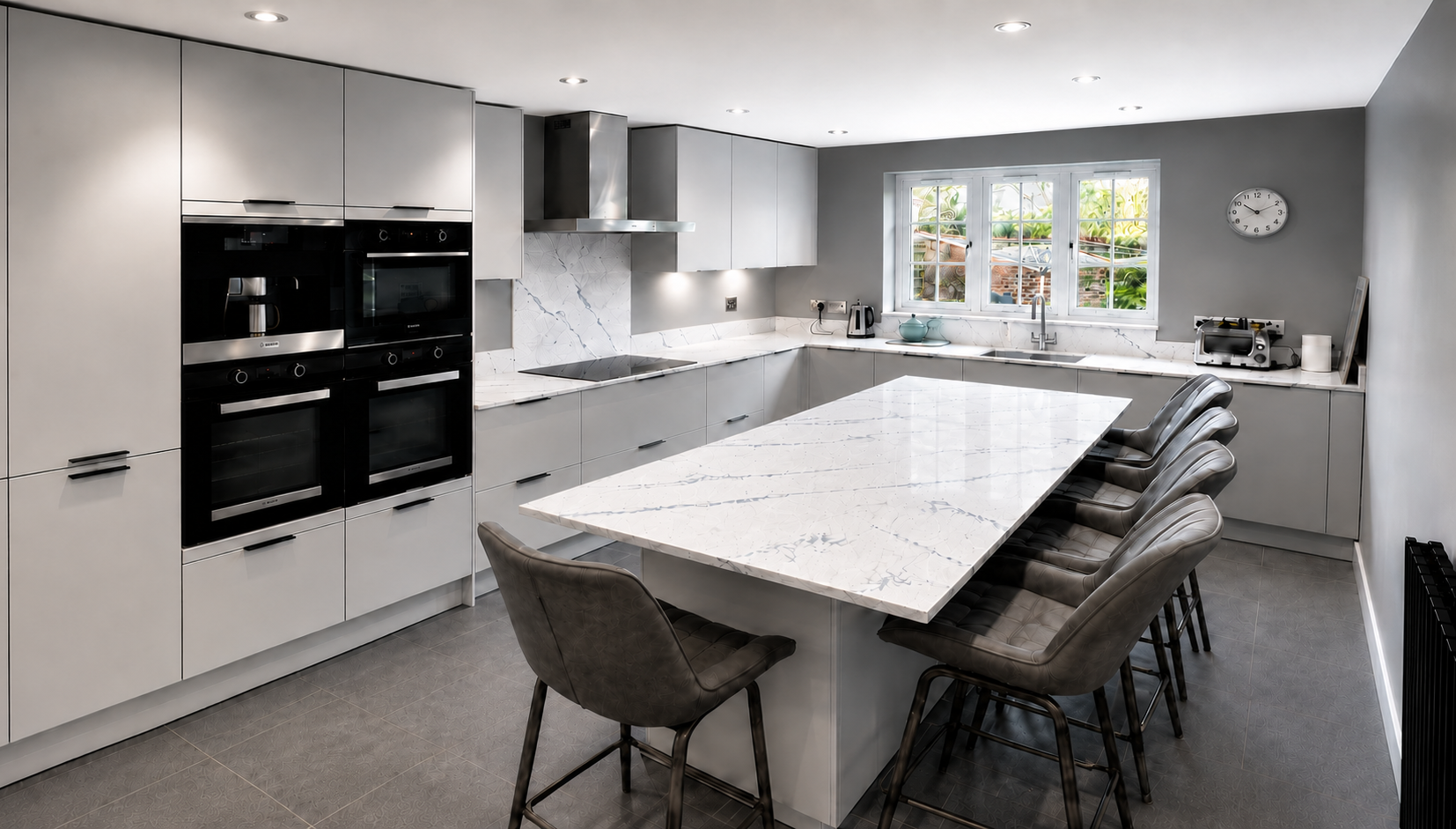 Modern grey kitchen in Wokingham with a large quartz island featuring deep blue veining, integrated ovens, induction hob and grey tiled flooring by Blacktail Kitchens.