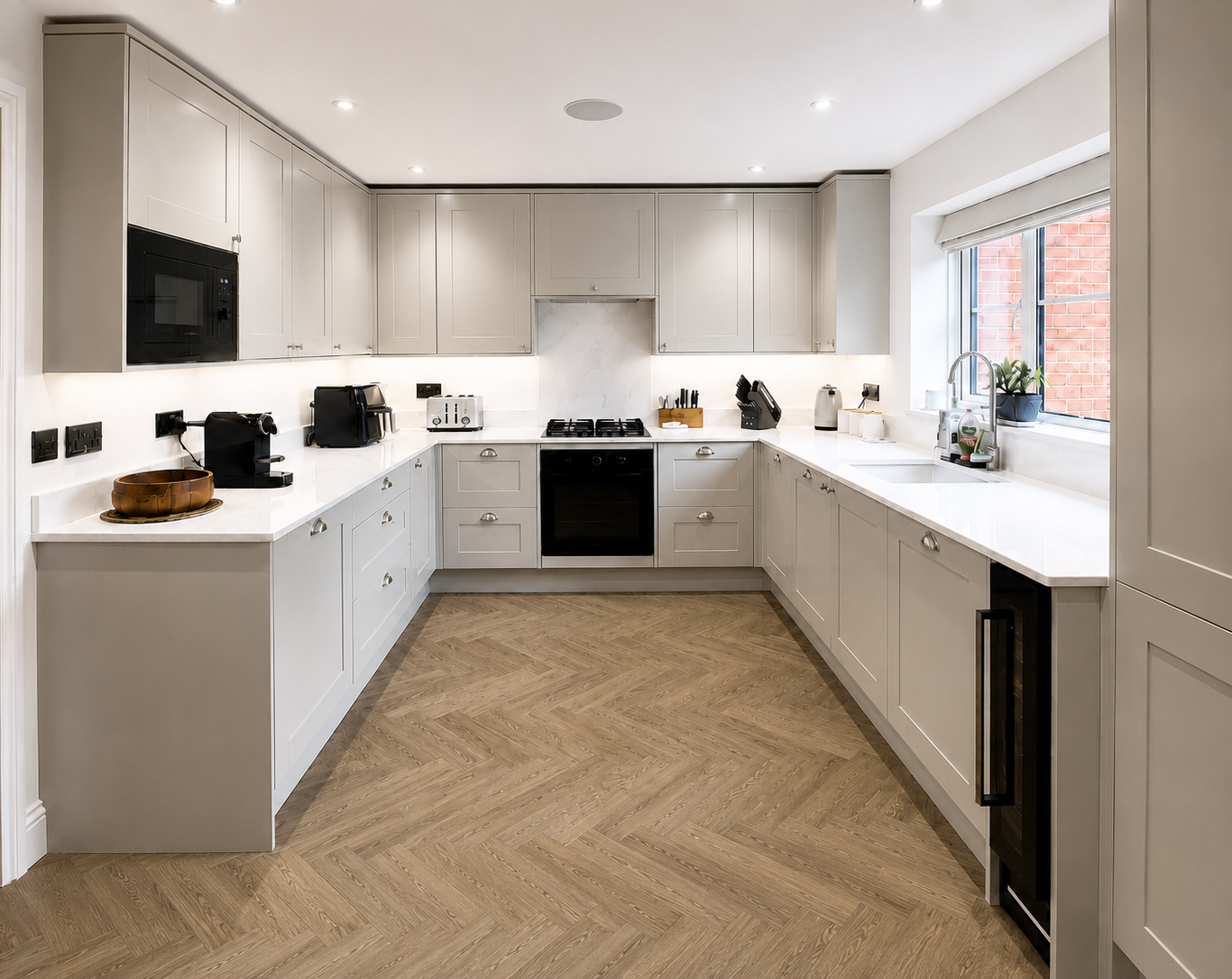 Modern kitchen with light grey cabinets, white quartz worktops, black appliances, undermount sink and herringbone flooring