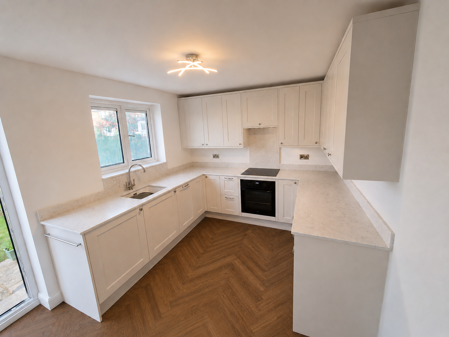 Completed shaker fitted kitchen in Ascot with quartz splashback, integrated oven and hob, tall storage, aligned cabinetry and dark herringbone LVT flooring.