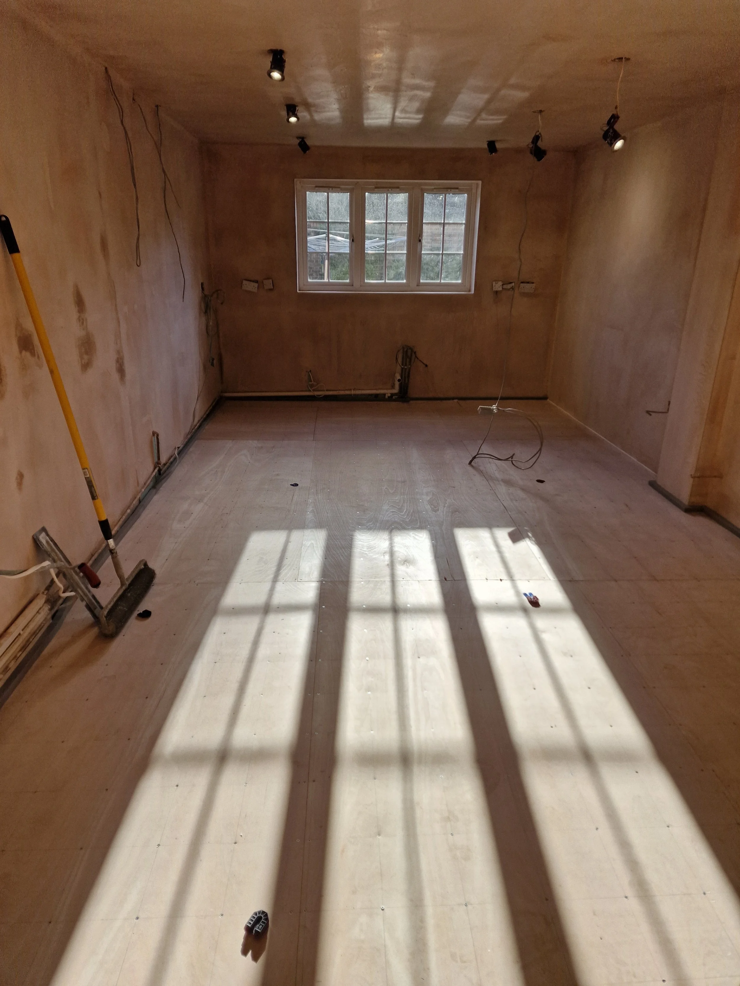 Empty room under construction with unfinished walls, a window letting in sunlight, and shadows cast on the floor.