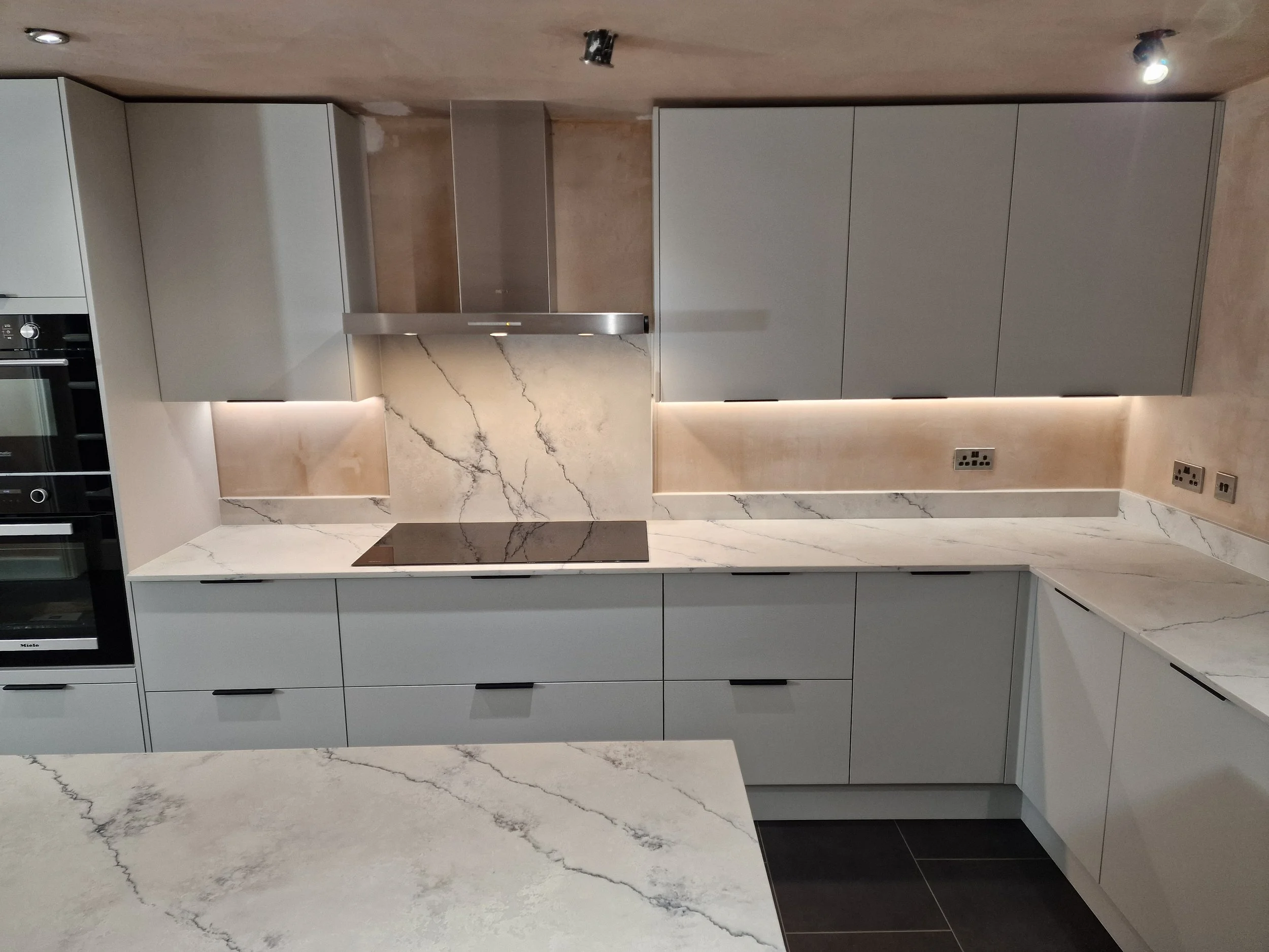 Modern kitchen with gray cabinets, marble countertops, backsplash with marble pattern, built-in oven, and electric cooktop, under-ceiling lighting
