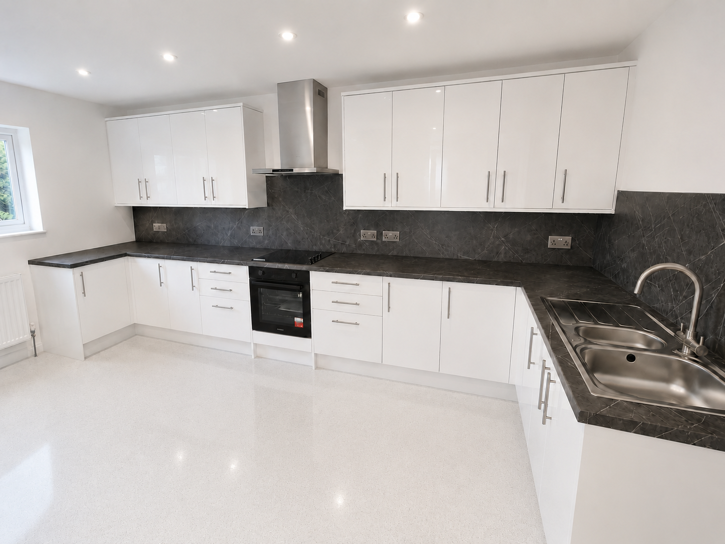 White gloss fitted kitchen in Crowthorne with stainless steel bar handles, double bowl sink, dark marble-effect splashbacks and carefully aligned cabinetry.
