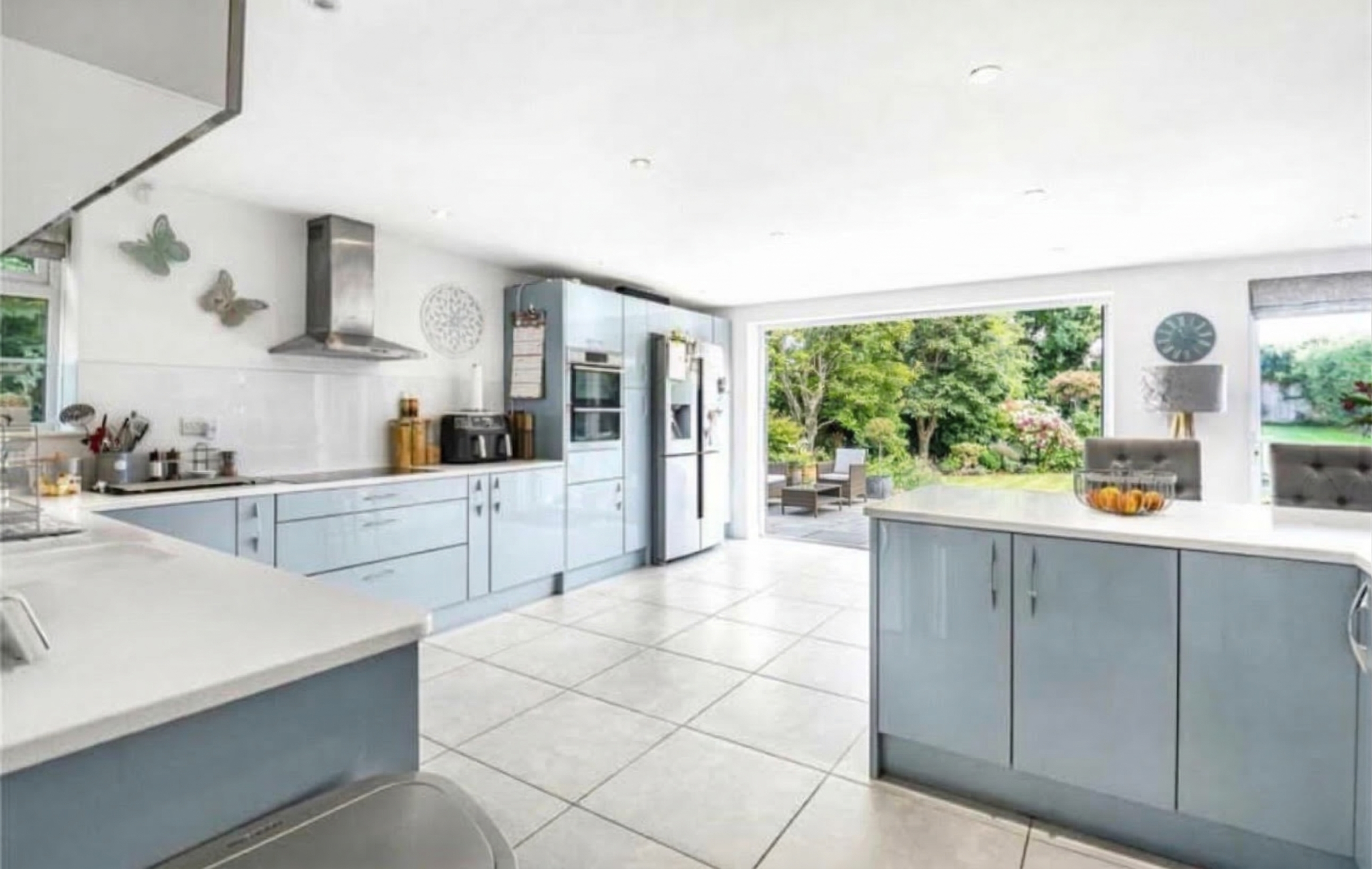Bright kitchen with light blue cabinets, white countertops, and large windows opening to a garden patio with outdoor seating.
