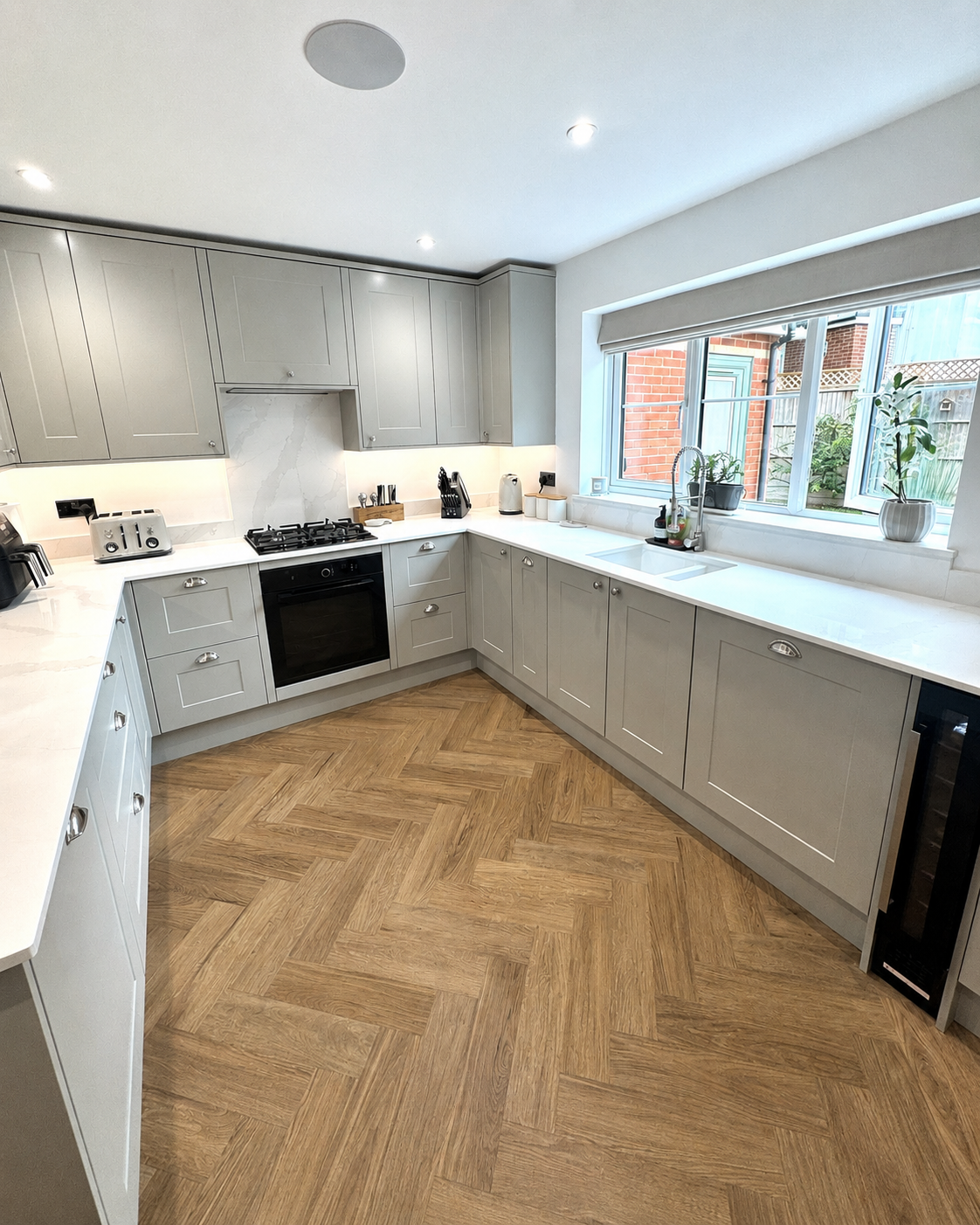 Completed grey shaker fitted kitchen in Reading with quartz worktops, integrated appliances, microwave housing, aligned cabinetry and herringbone LVT flooring.