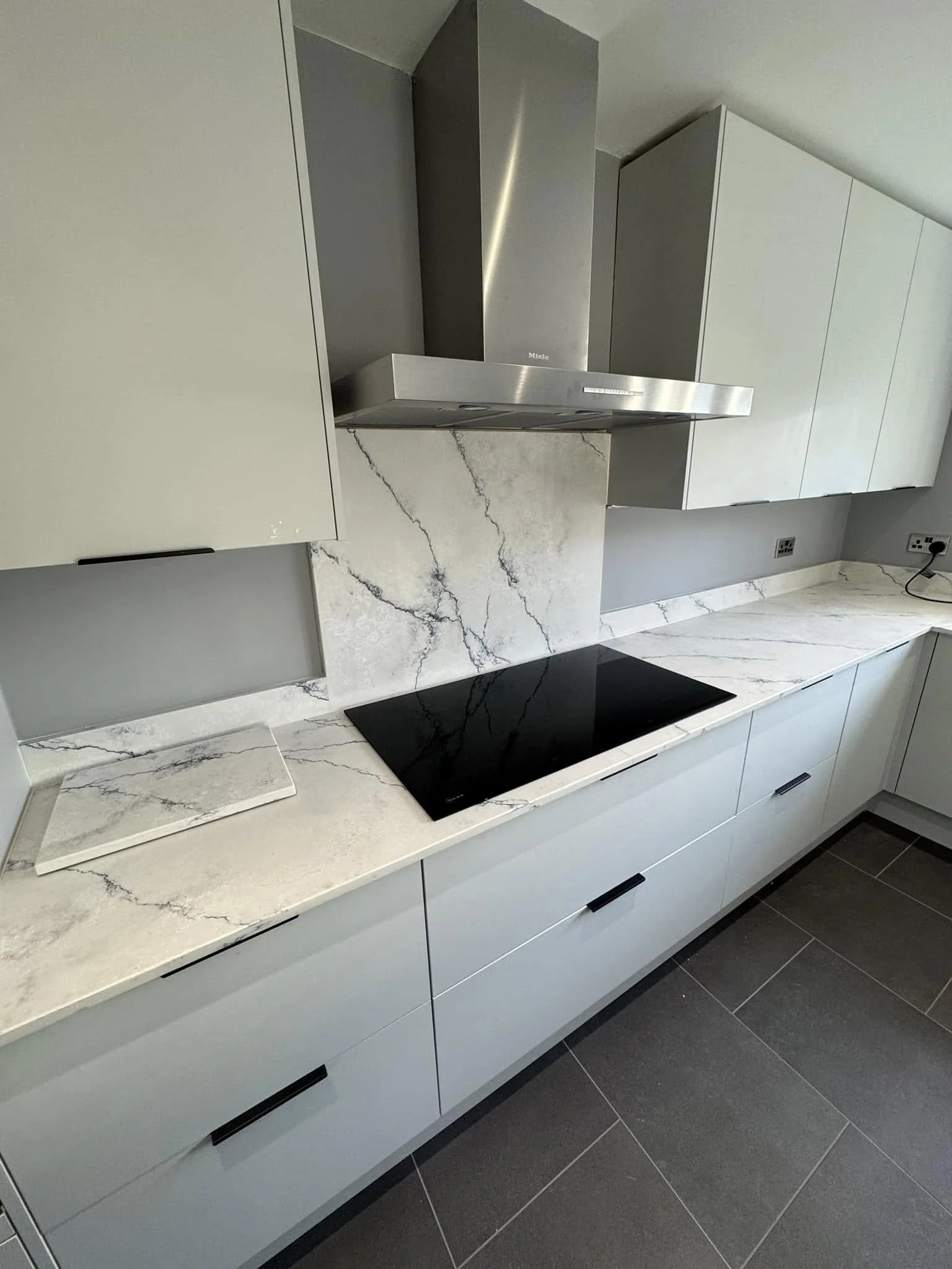 Modern kitchen with white cabinets, marble countertops, and a black electric stove, with a stainless steel range hood.