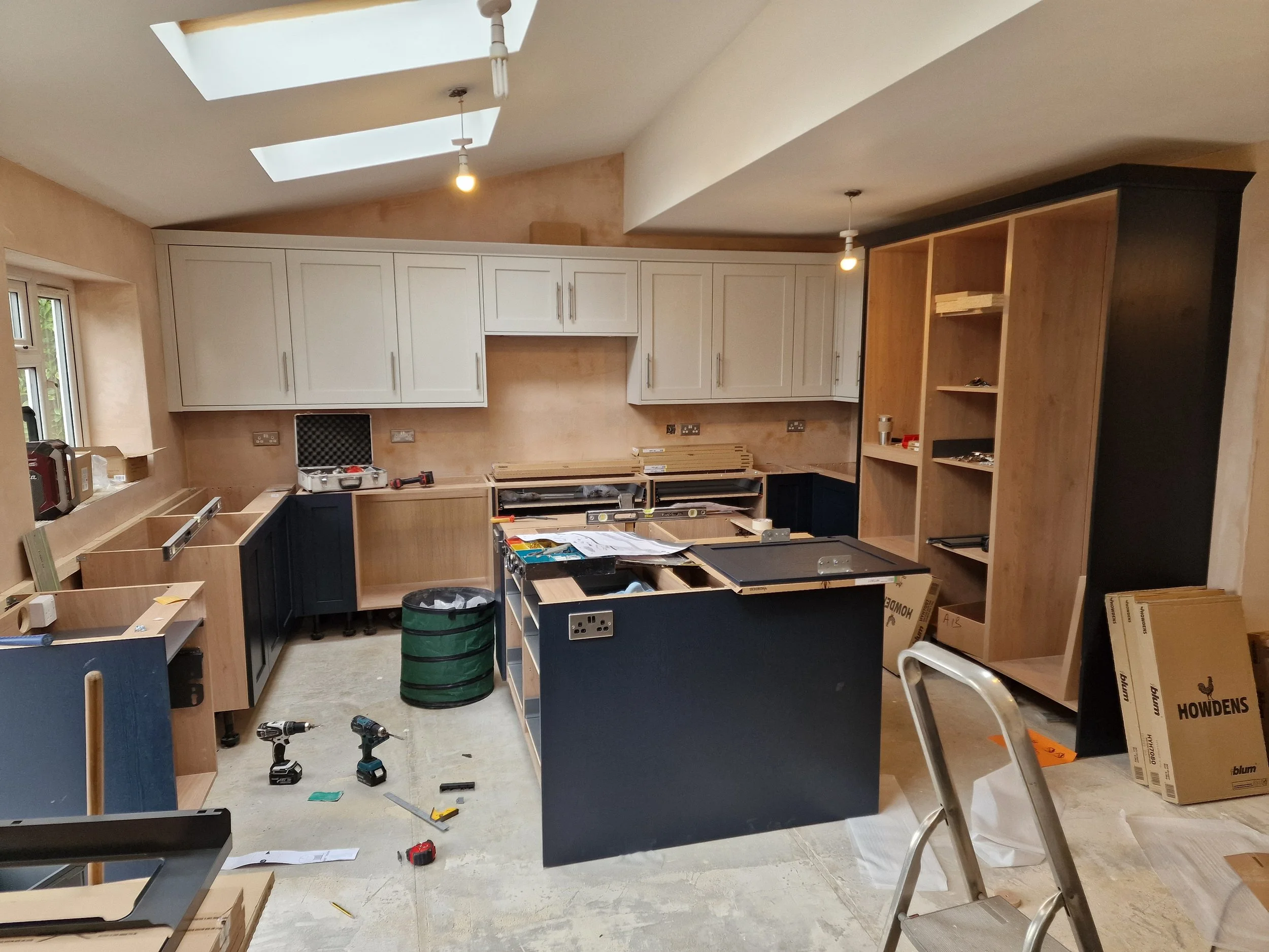 Kitchen preparation before installation with unfinished cabinetry, tools, and construction materials scattered around.