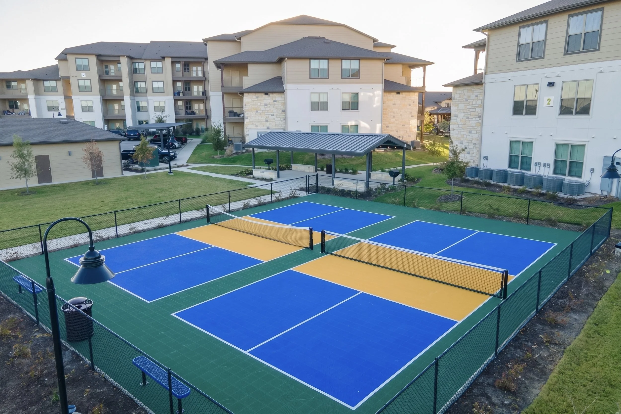 Colorful outdoor tennis courts surrounded by apartment buildings with parking lot and landscaped areas.