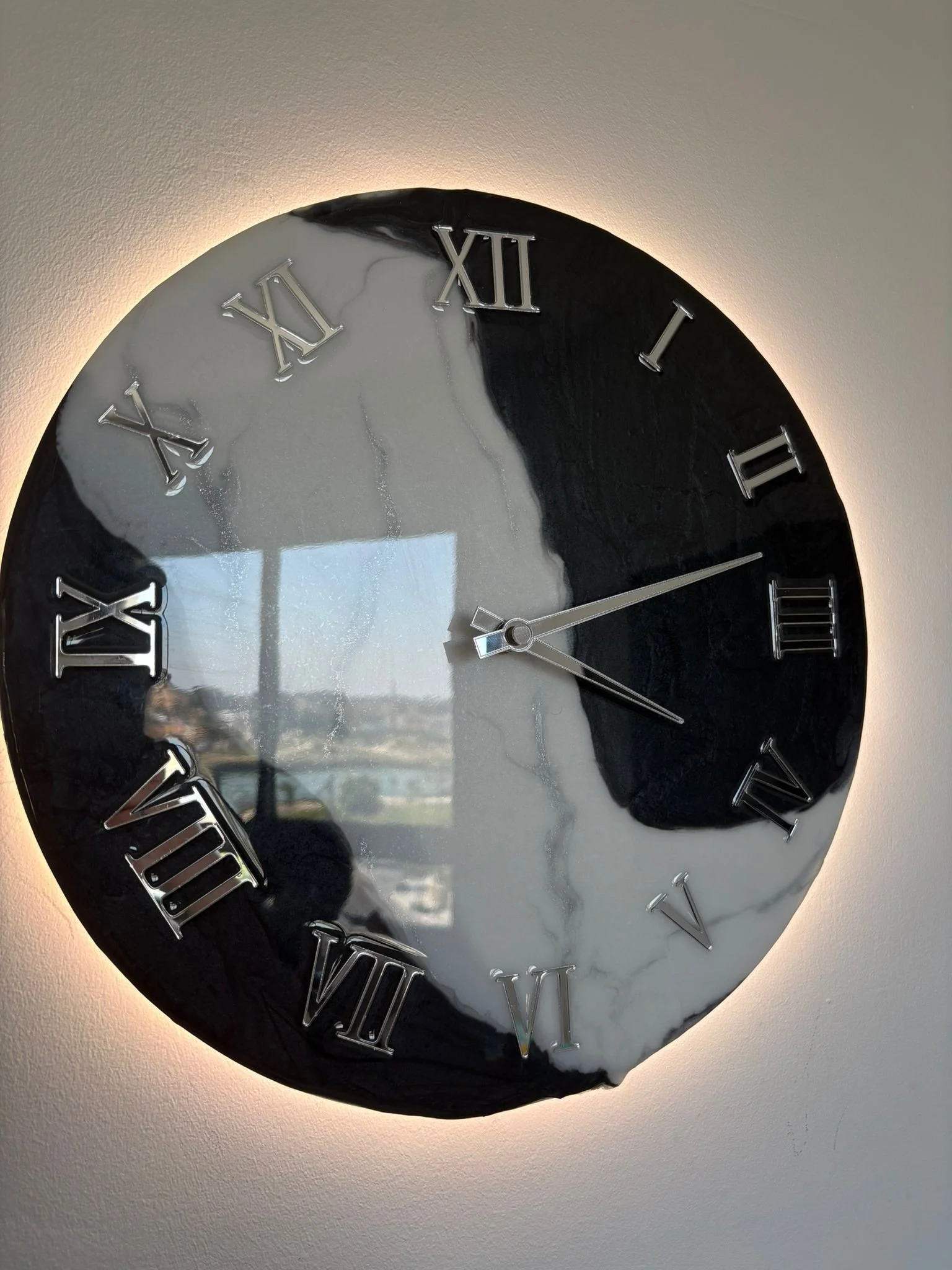 Round wall clock with black and white marble pattern, silver Roman numerals, and silver hands, illuminated from behind.