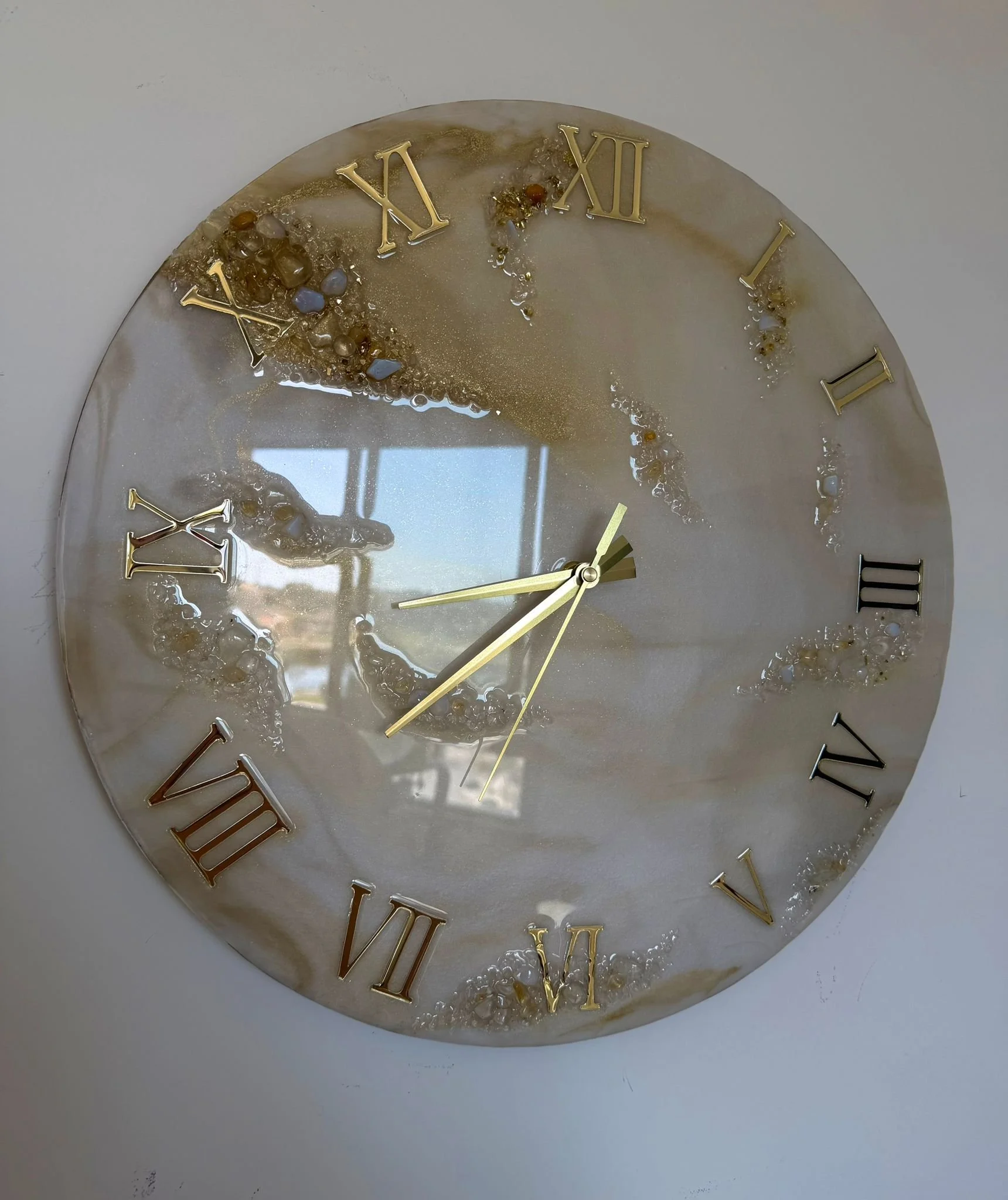 Decorative wall clock with gold Roman numerals and a marble-like face, reflecting a window and sky.