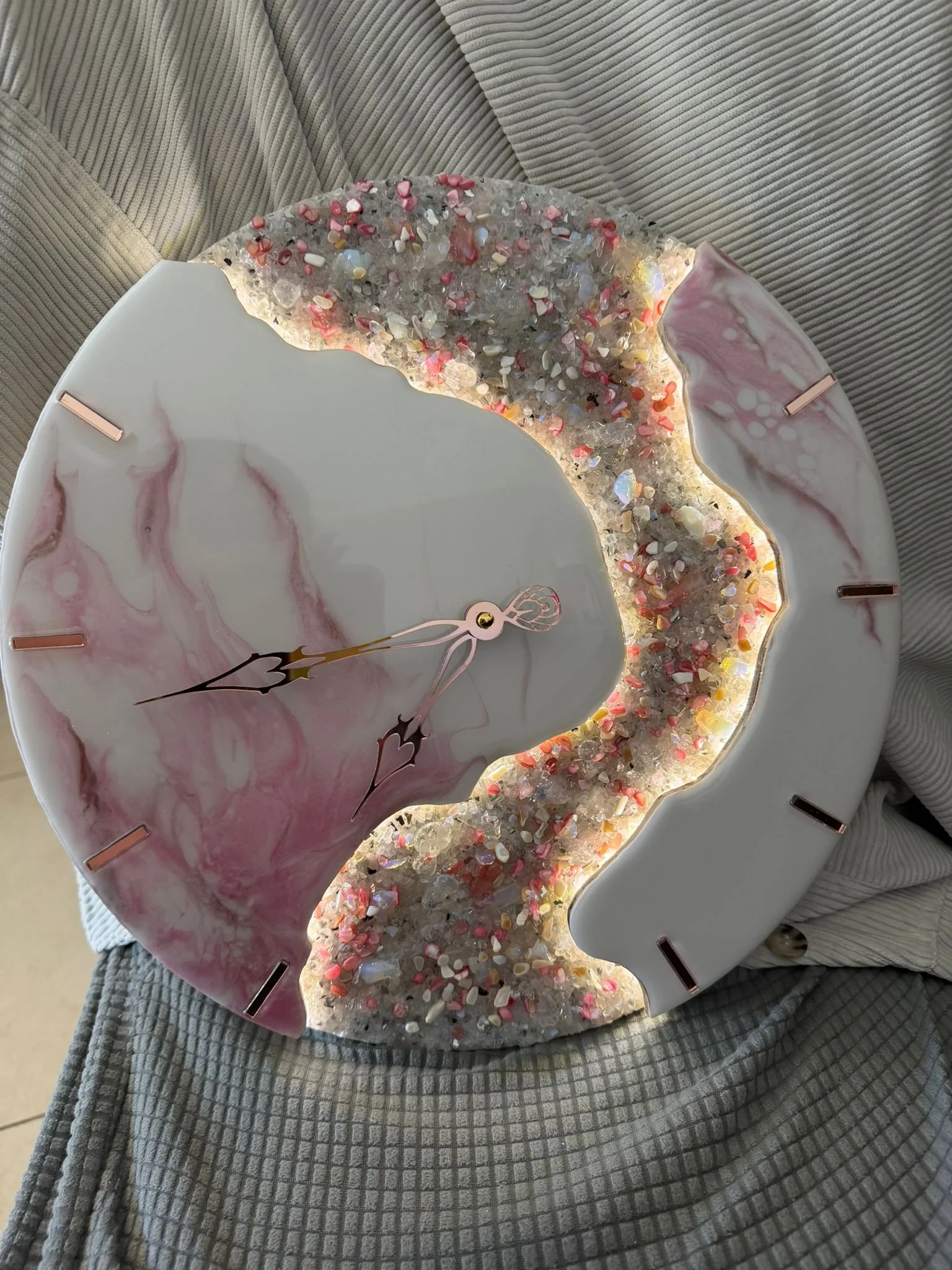 A decorative wall clock with pink and white marbled design and a glittery, textured border with colorful stones and embedded lights.