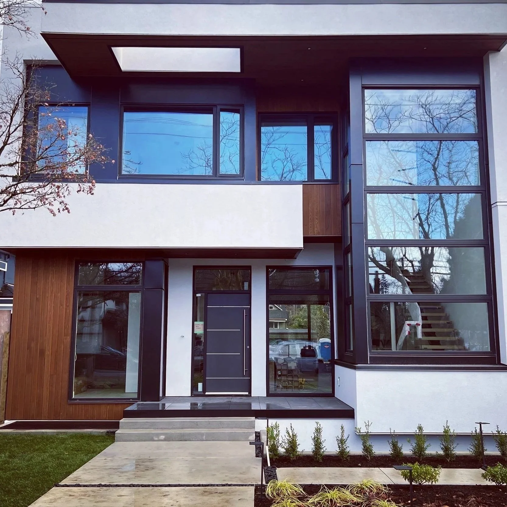 Modern two-story house with large windows, wooden accents, and a front porch with steps leading to the entrance.
