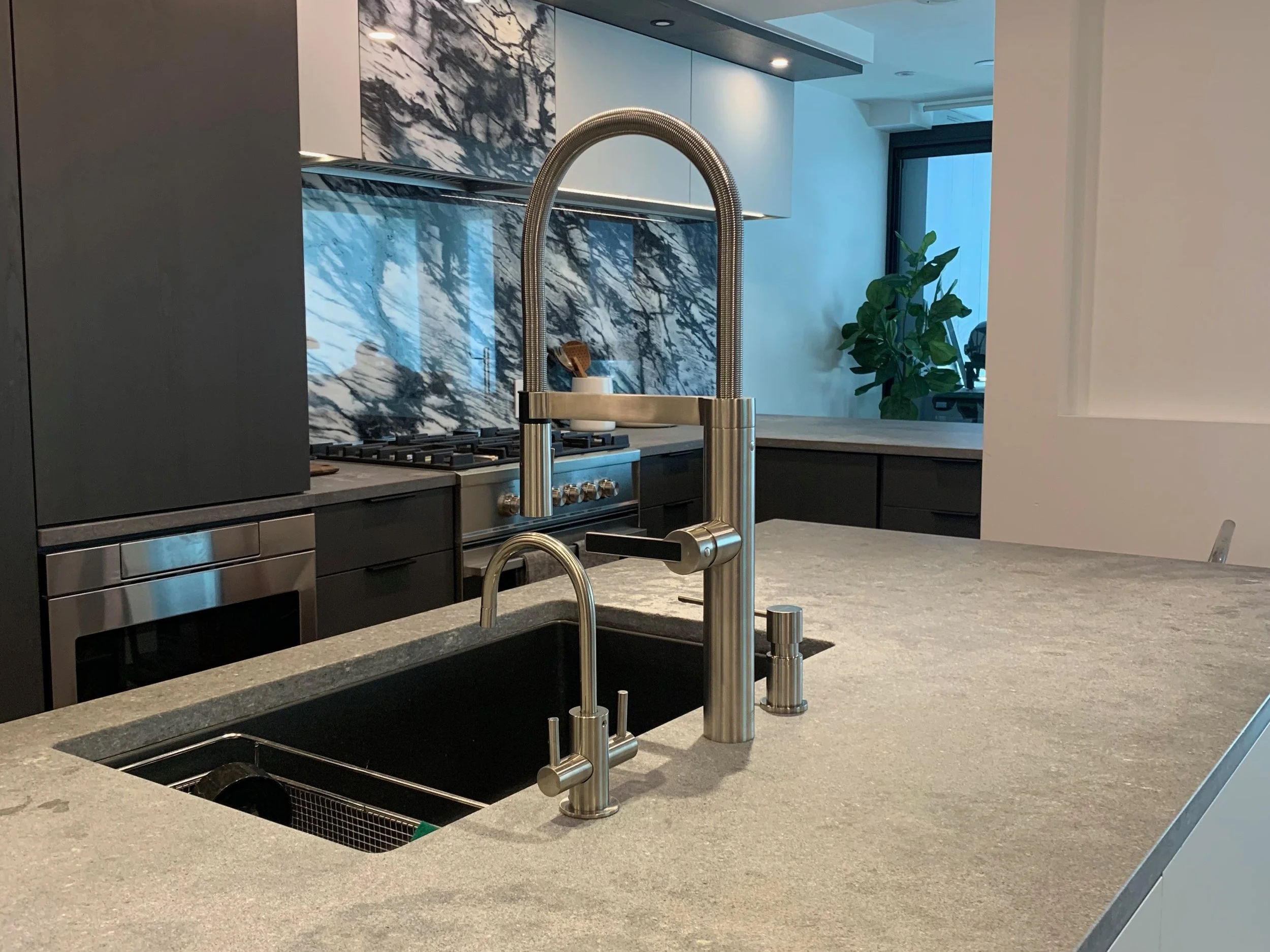 Modern kitchen with marble backsplash, stainless steel faucet, black undermount sink, and gray countertop