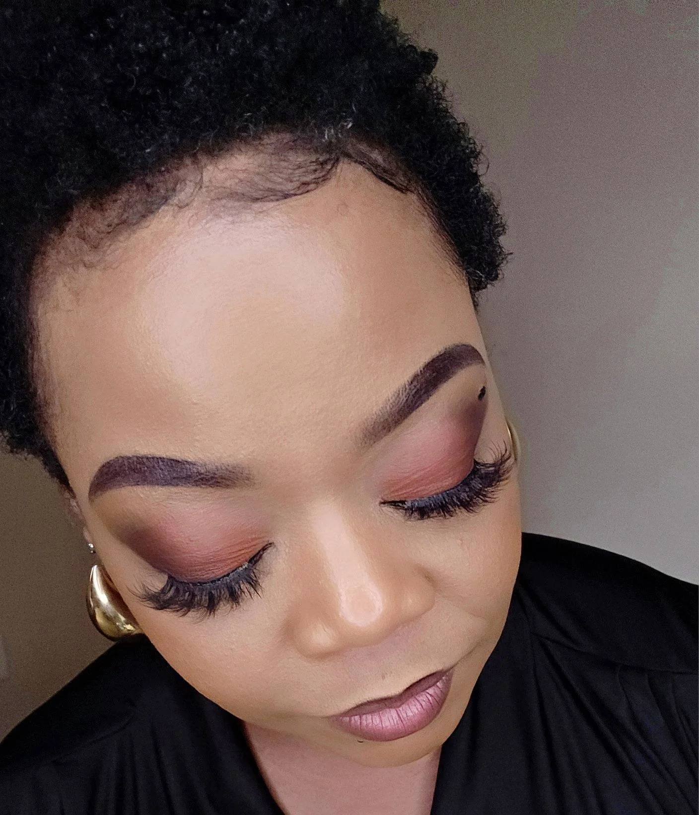 Close-up of a woman's face with her eyes closed, showcasing her makeup and short curly black hair.