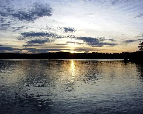 Sunrise with sun and clouds reflected in the water.
