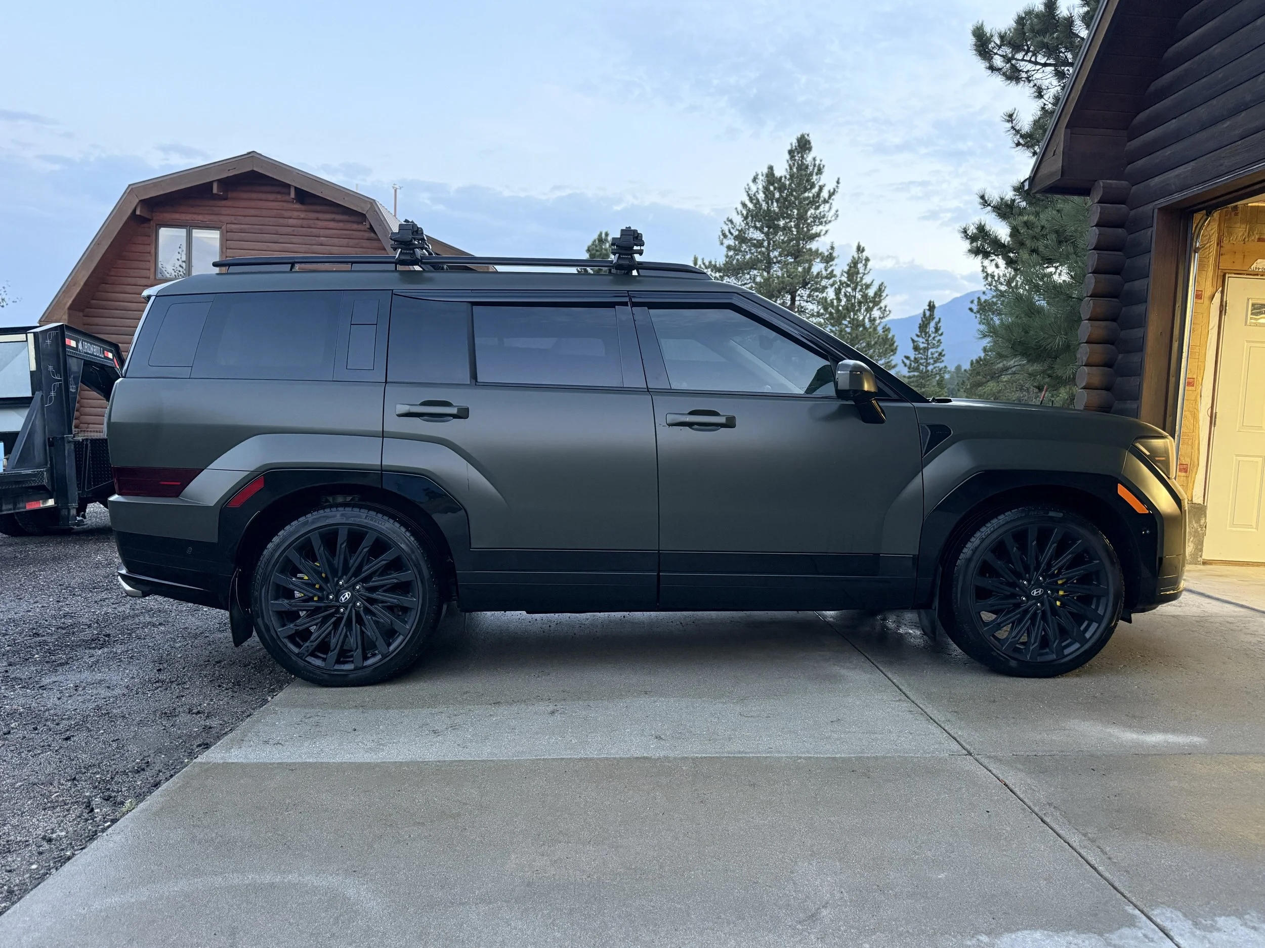 Black modern SUV vehicle parked in driveway in front of a house with mountain scenery in the background.