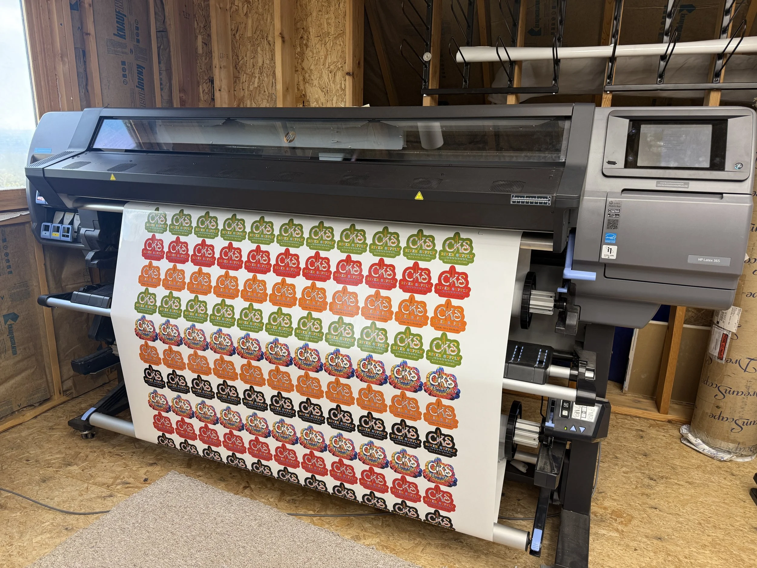 Large-format printer printing sheets of colorful stickers with various logos and designs.