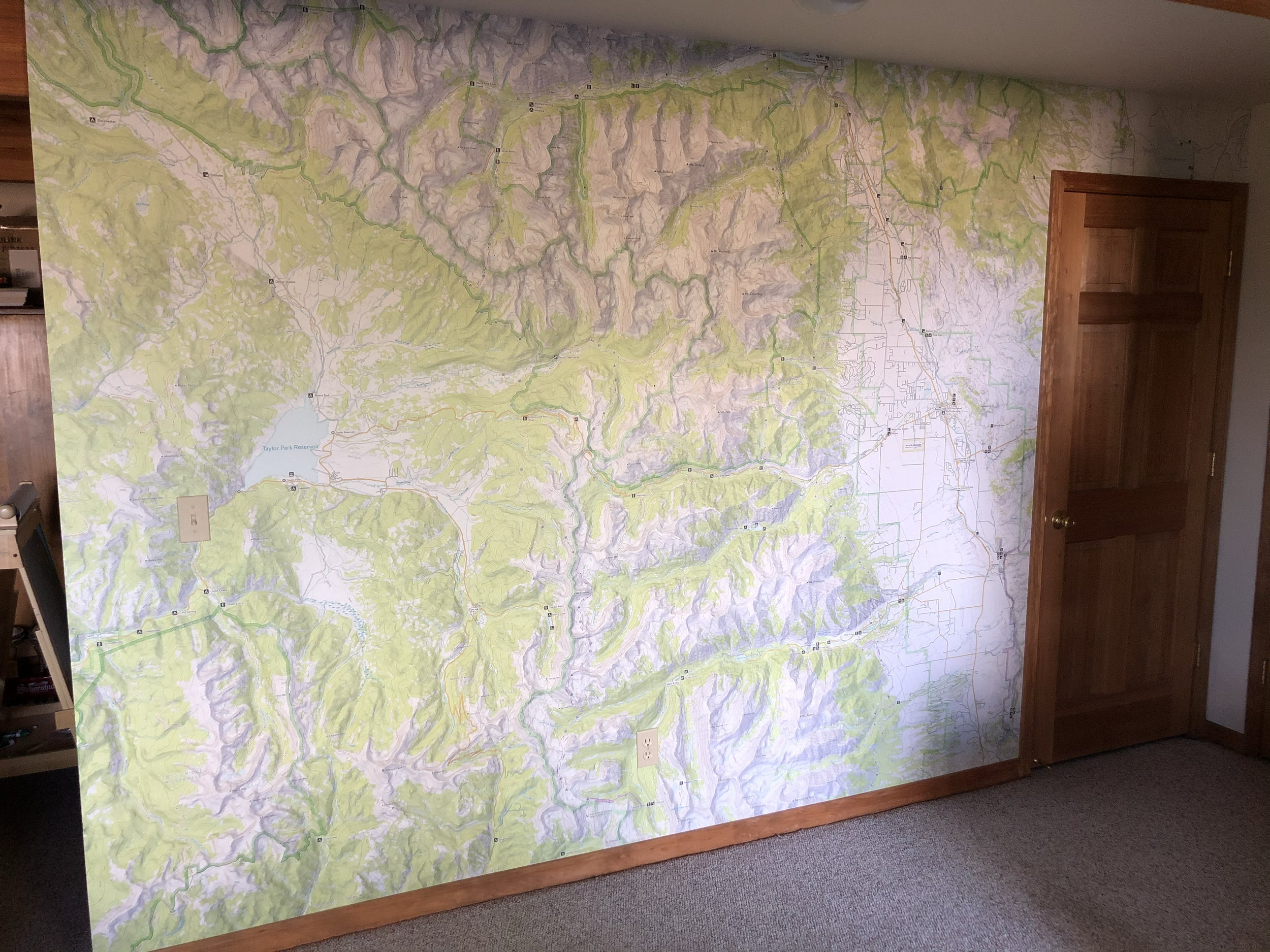 A large, detailed topographic map on a wall, depicting hills, valleys, roads, and a reservoir in a mountainous area.