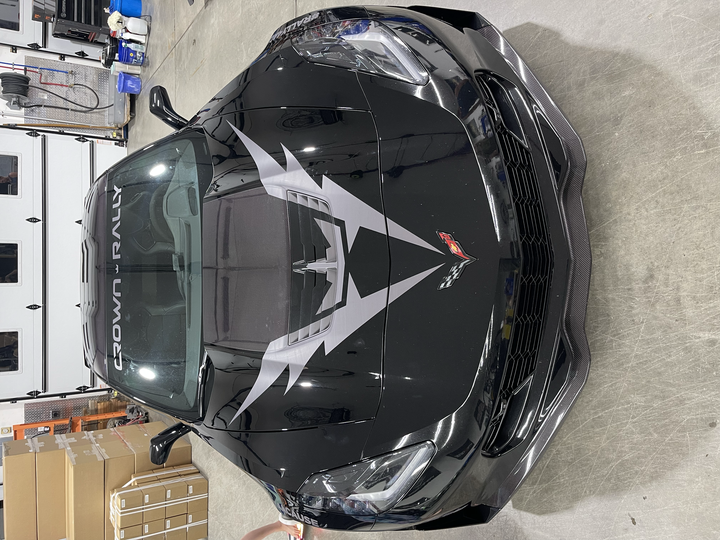 A black Chevrolet Corvette Z06 sports car with a racing-inspired decal design on the hood, parked inside a garage.