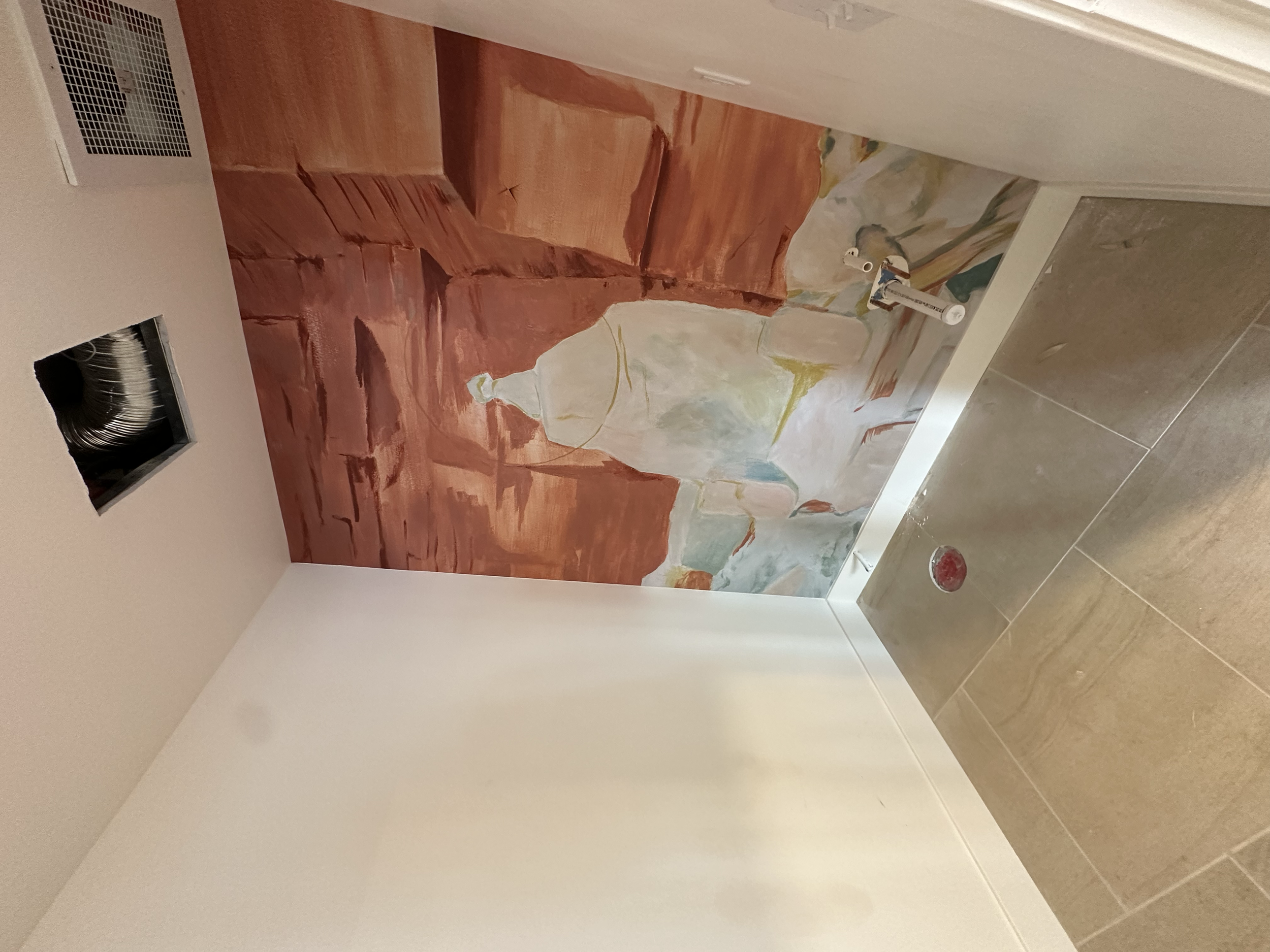 An unfinished bathroom with a painted mural on the back wall depicting a woman in a flowing dress, with construction tools and materials still present.