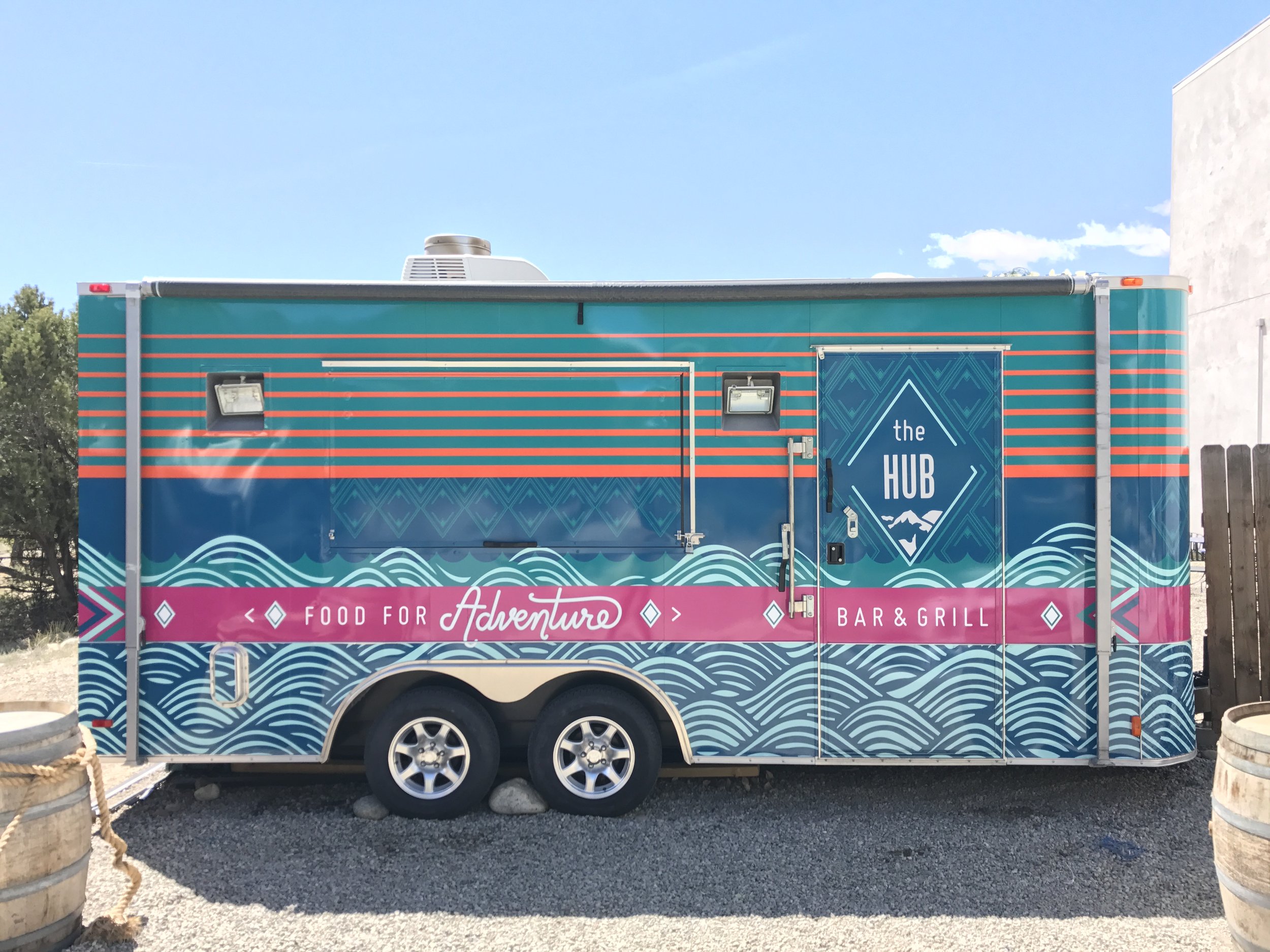 Colorful food truck with blue and pink design, text reading "food for adventure," and a logo that says "the HUB."