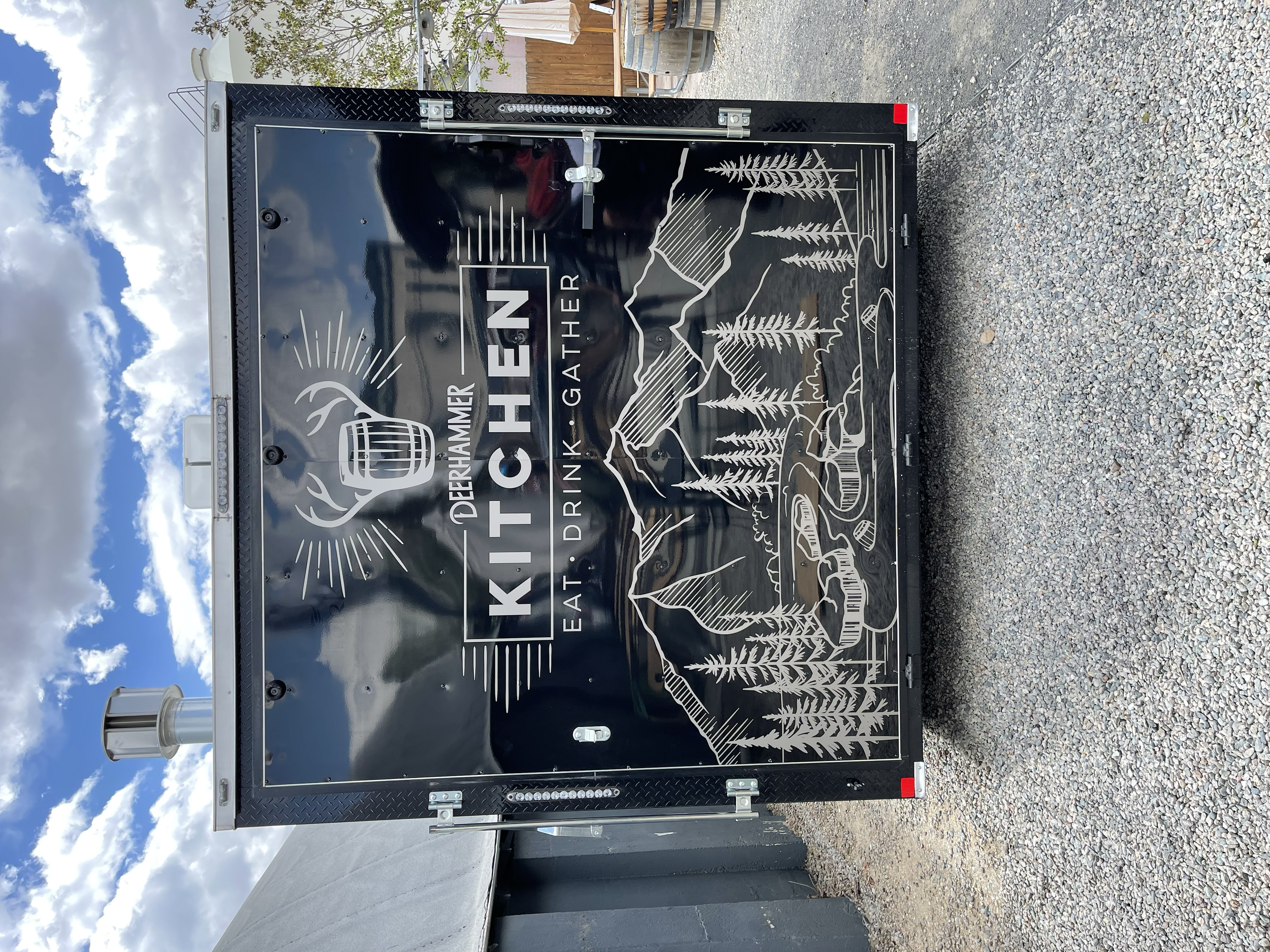 Black food truck with mountain and pine tree illustrations and the text 'The Derflamier Kitchen Eat, Drink, Gather'.