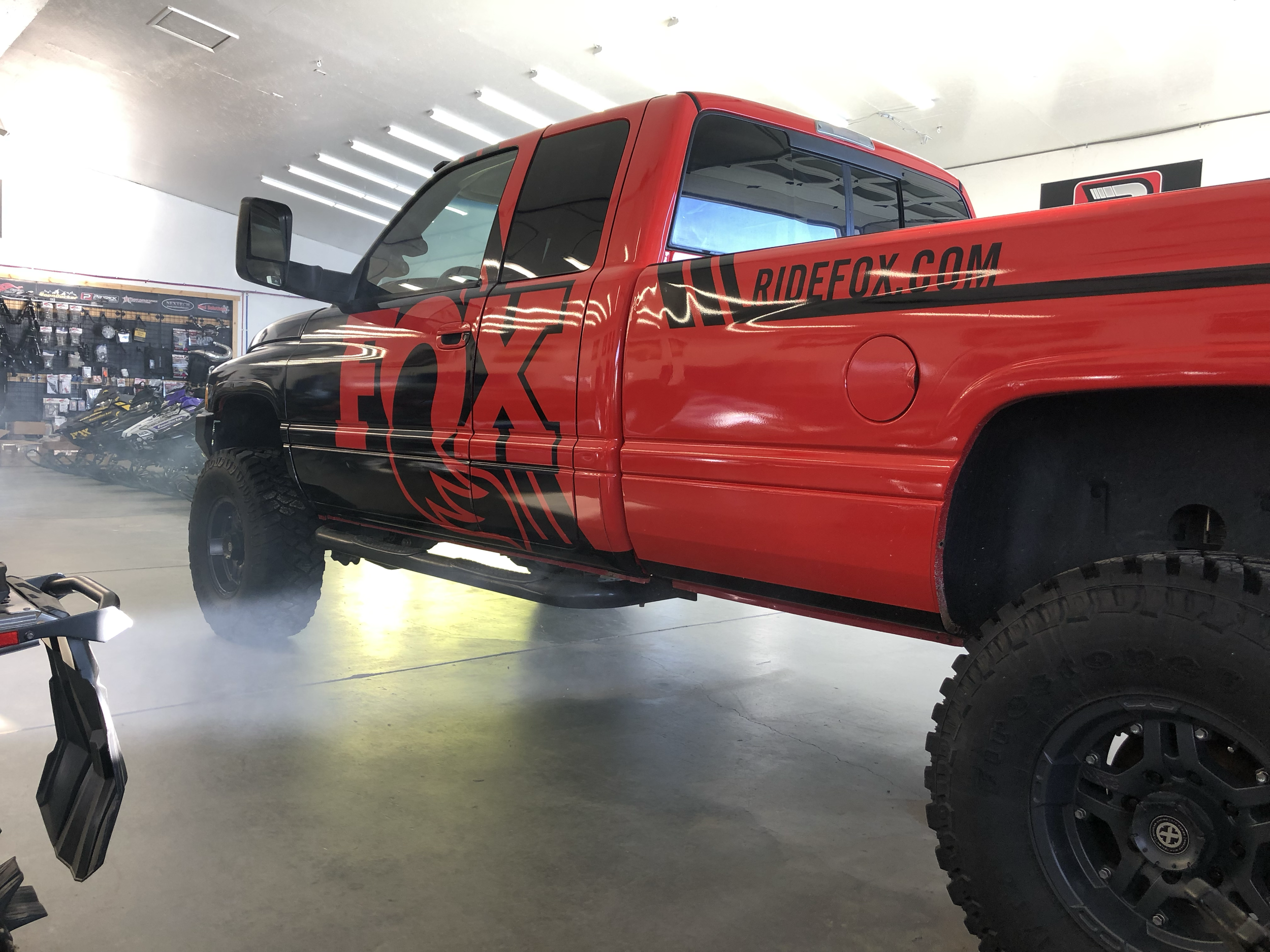 Red and black pickup truck inside a garage with racing graphics and the URL ridefox.com