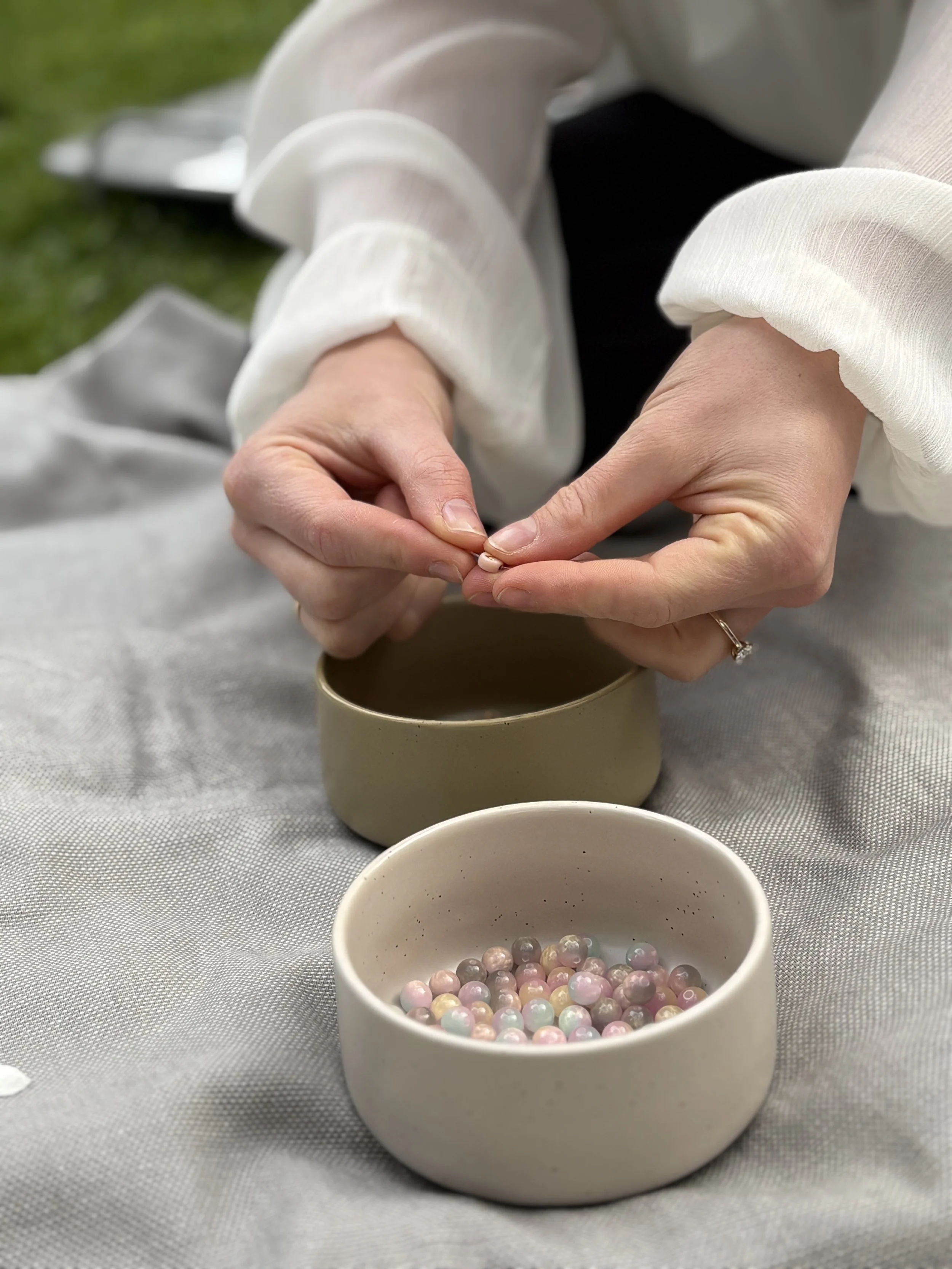 Close-up of a person holding a string of small, round pastel-colored beads, with open, empty bowls in the foreground and background, on a metallic surface.
